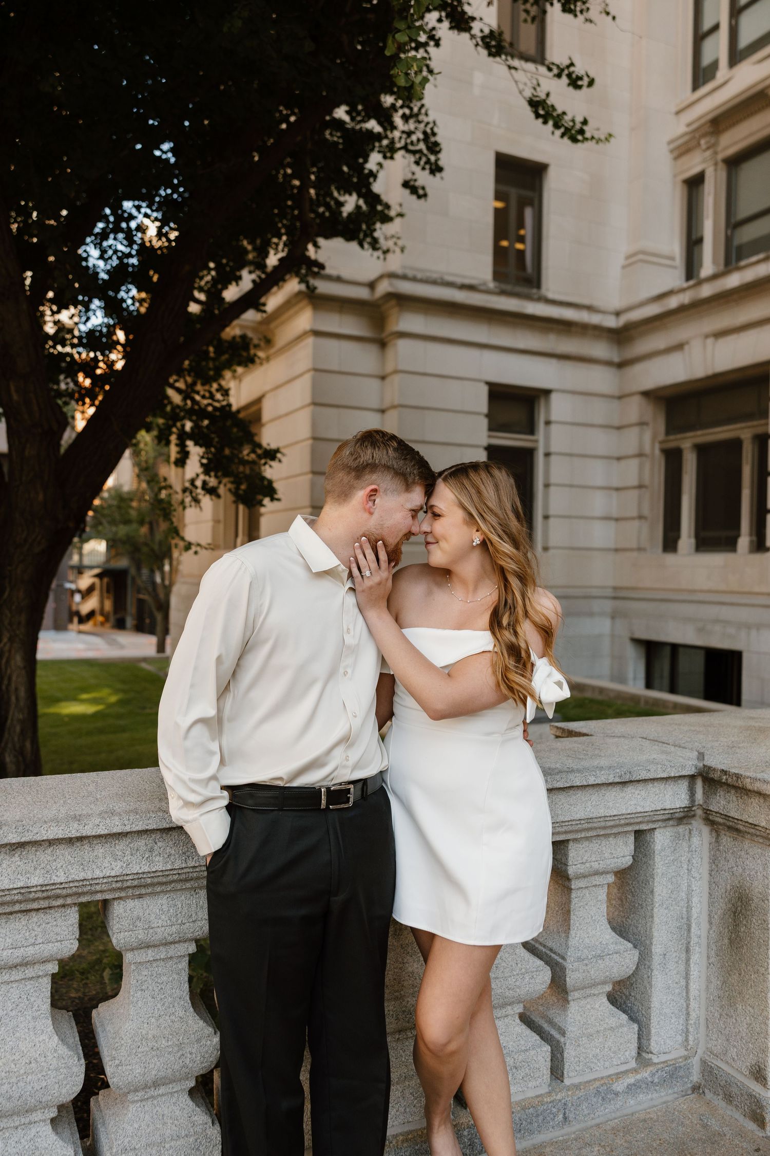 Romantic couple in formal wear embracing on stone balcony.