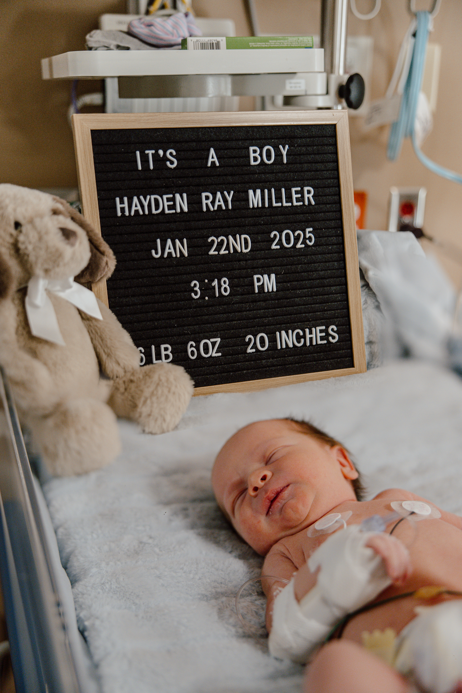 Hospital room scene with letterboard displaying newborn's birth details and sleeping baby.