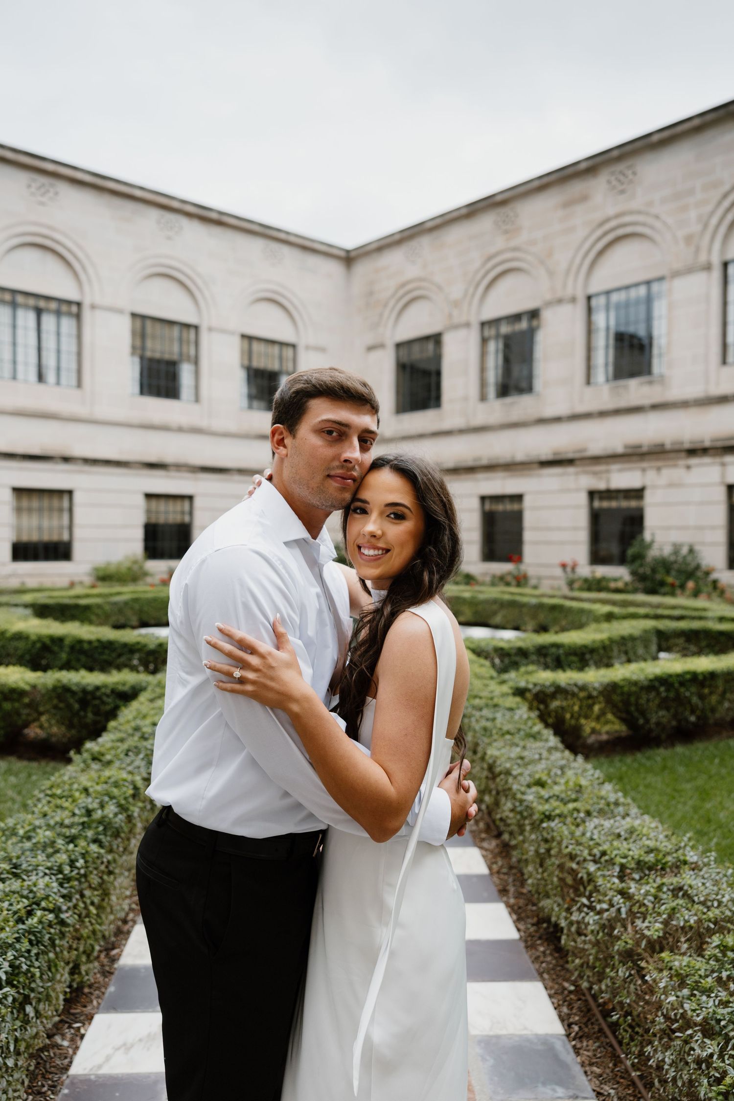 Romantic couple embraces in courtyard with classical white stone architecture.