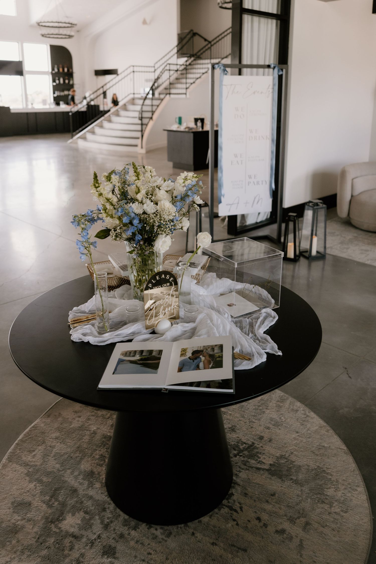 A modern black round table with white linens and delicate floral arrangements in a minimalist industrial space.