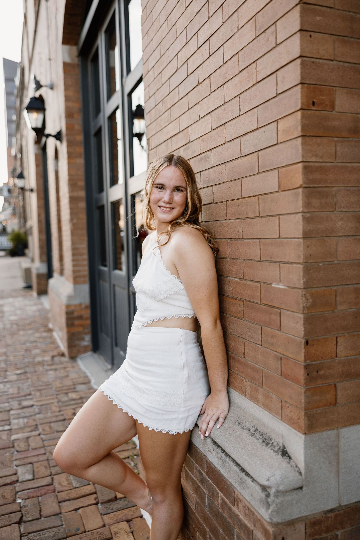 A white two-piece lace outfit photographed against a brick wall and cobblestone street.