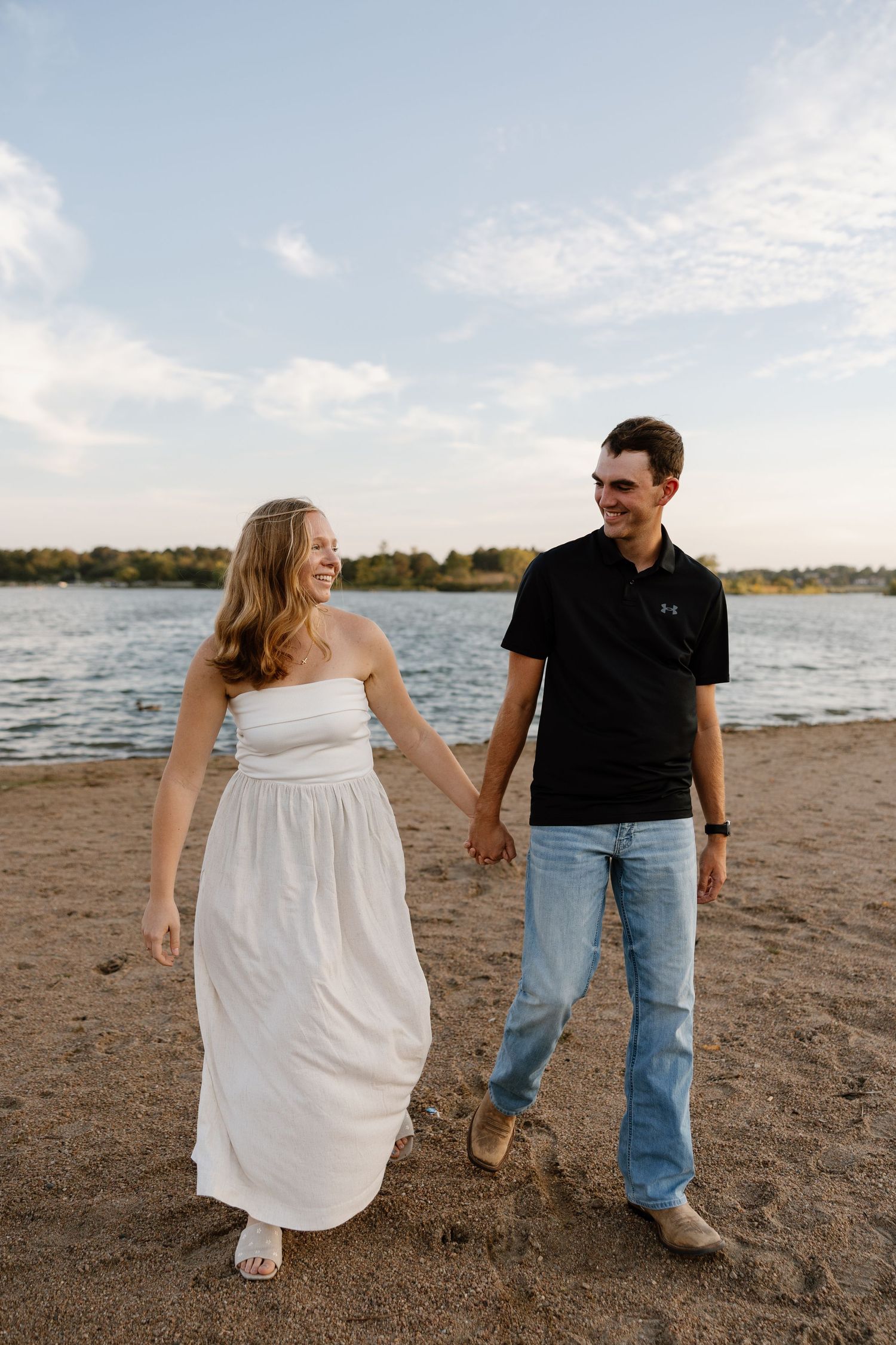 Couple walks hand in hand along a beach shoreline during a summer evening.