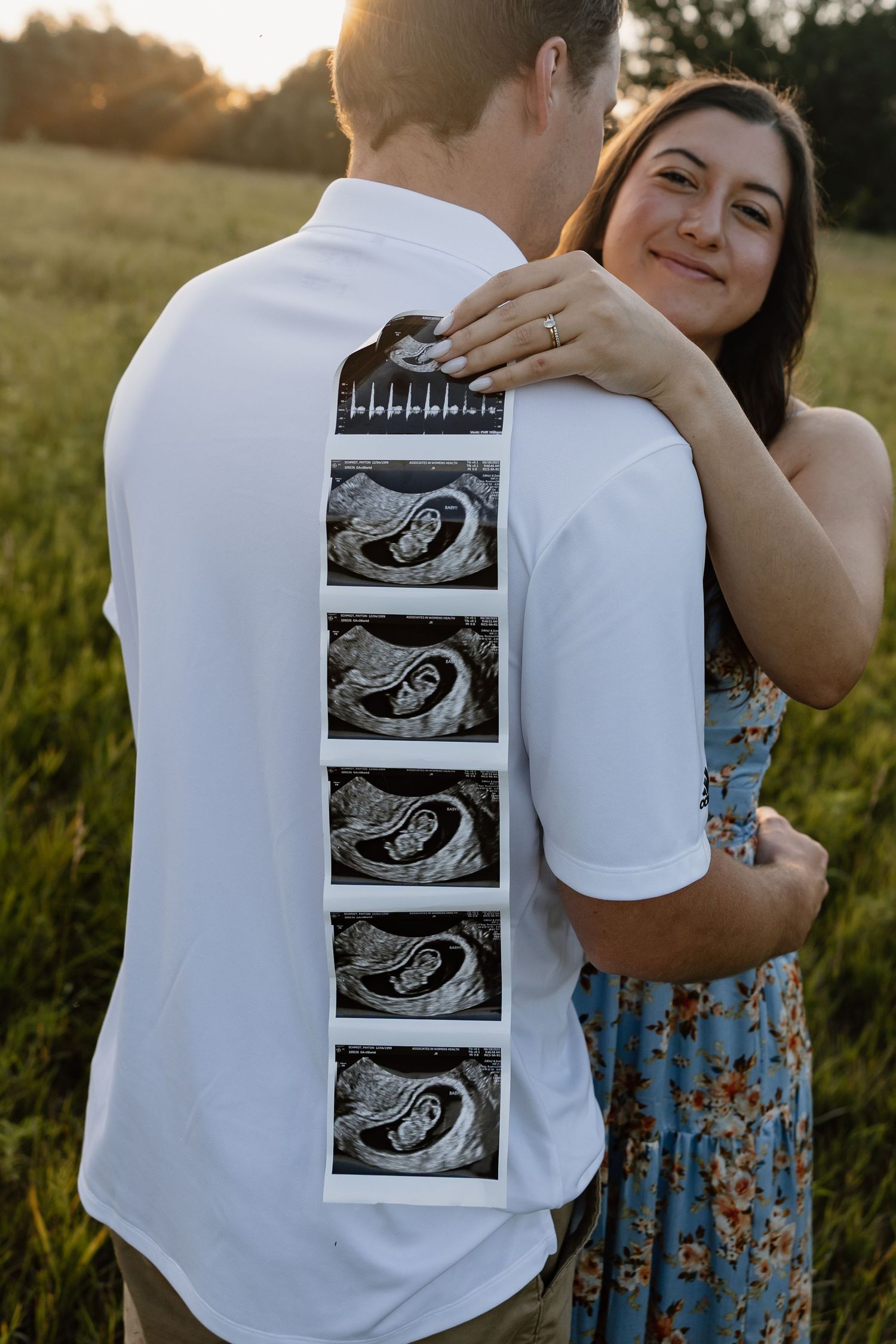Couple holding ultrasound photos during outdoor maternity photo session at golden hour.