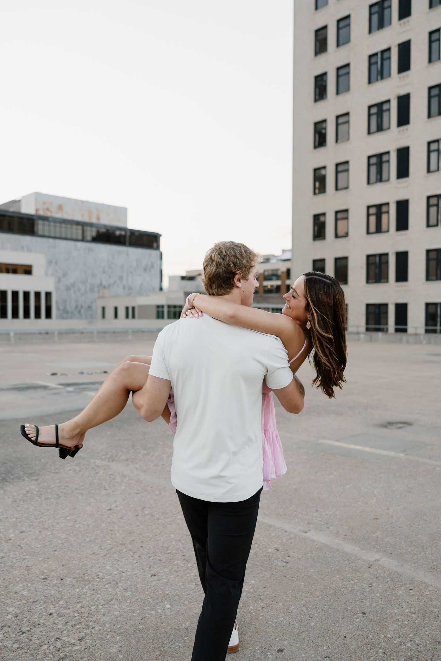 A playful couple embraces on a rooftop with urban architecture in the background.