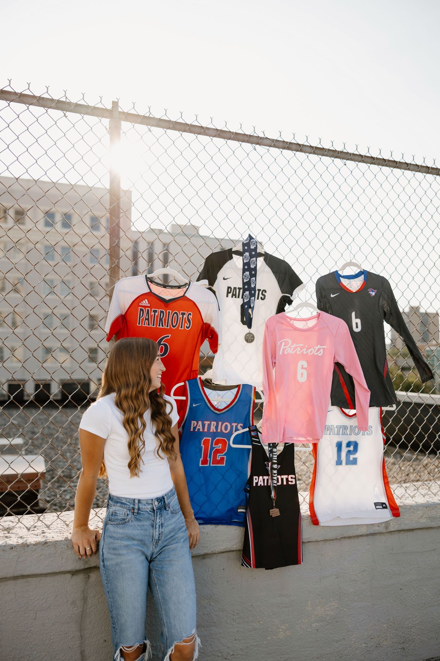 Sports jerseys and uniforms displayed on a chain link fence against a bright background.