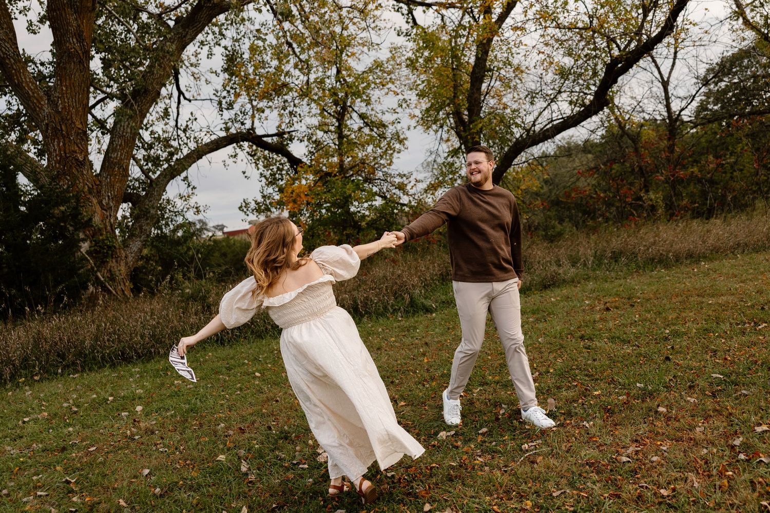 Couple dancing and twirling in a grassy field during autumn.