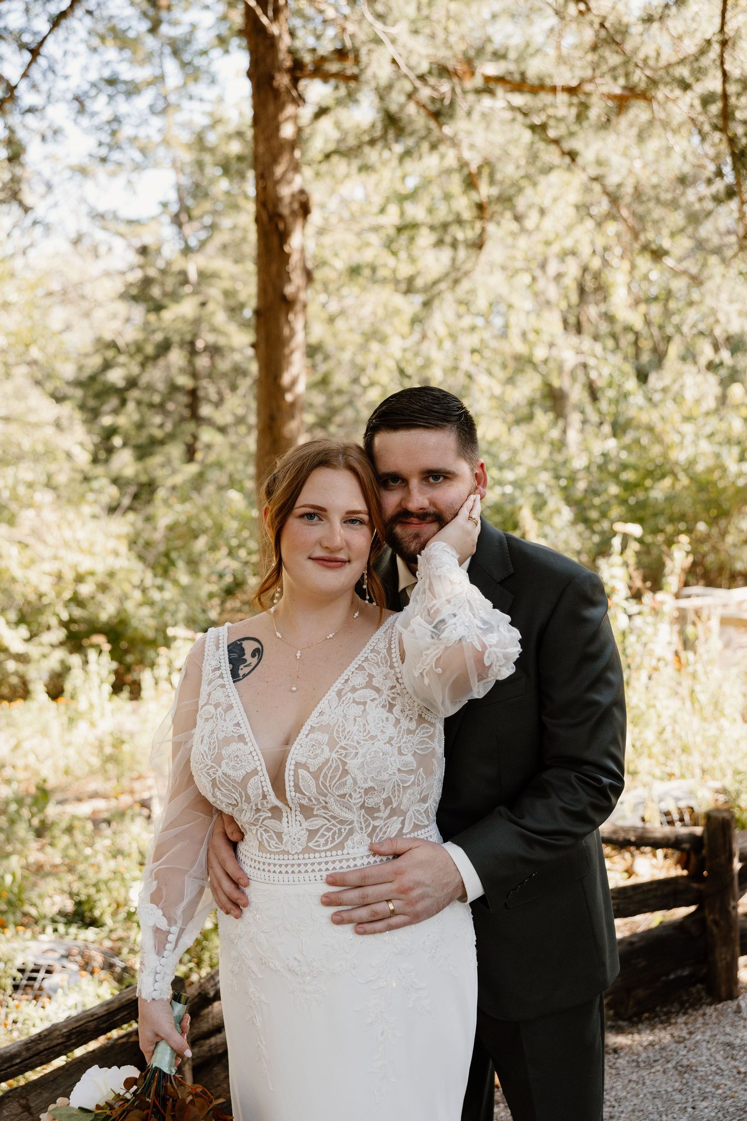 Wedding couple embracing in a forest setting with sunlight filtering through pine trees.