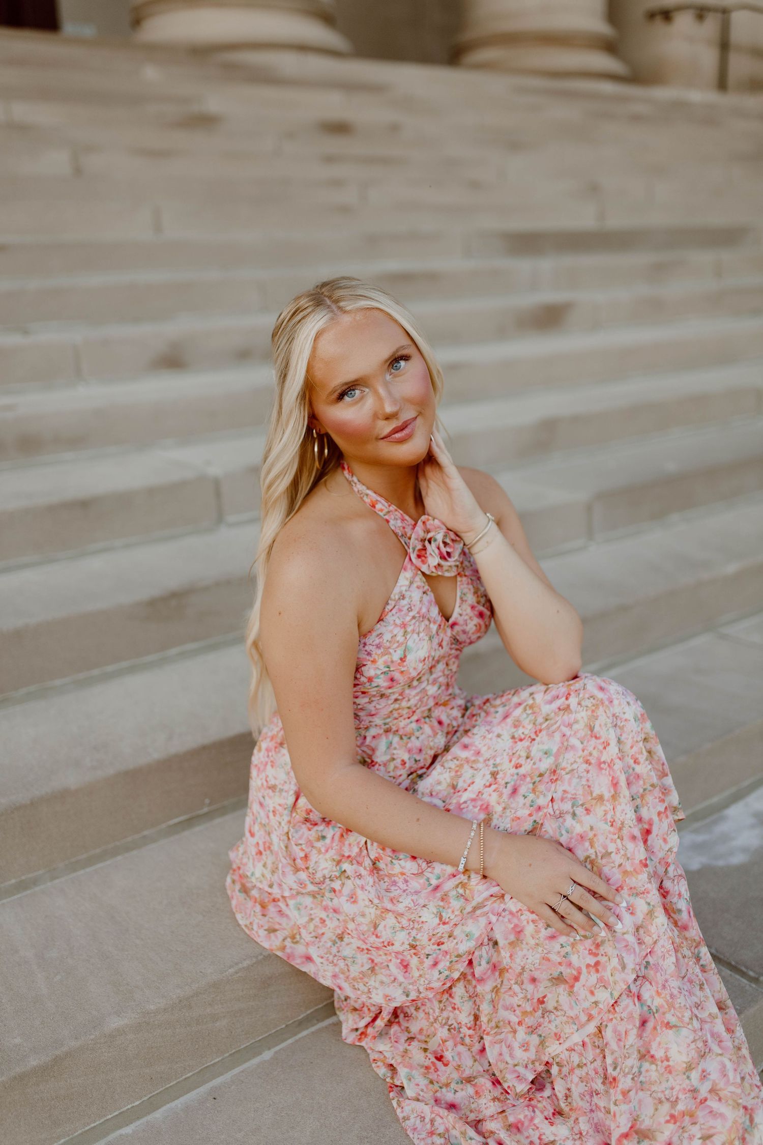Person in a flowing pink floral dress poses gracefully on stone steps.