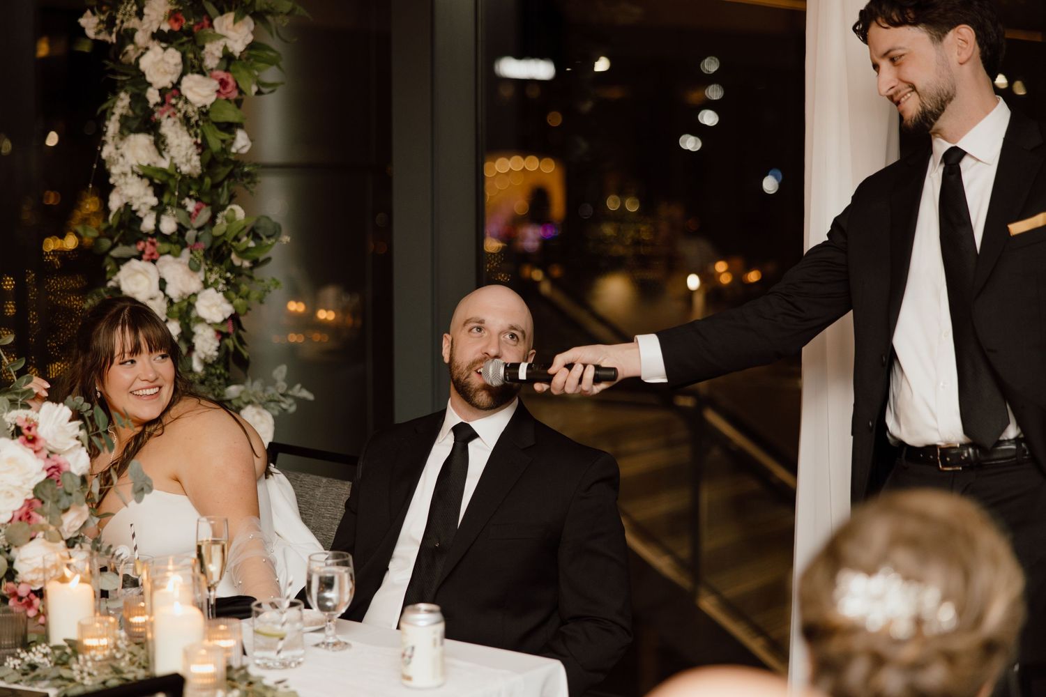 Wedding reception shows candid moment between guests during dinner speeches at an elegantly decorated venue.