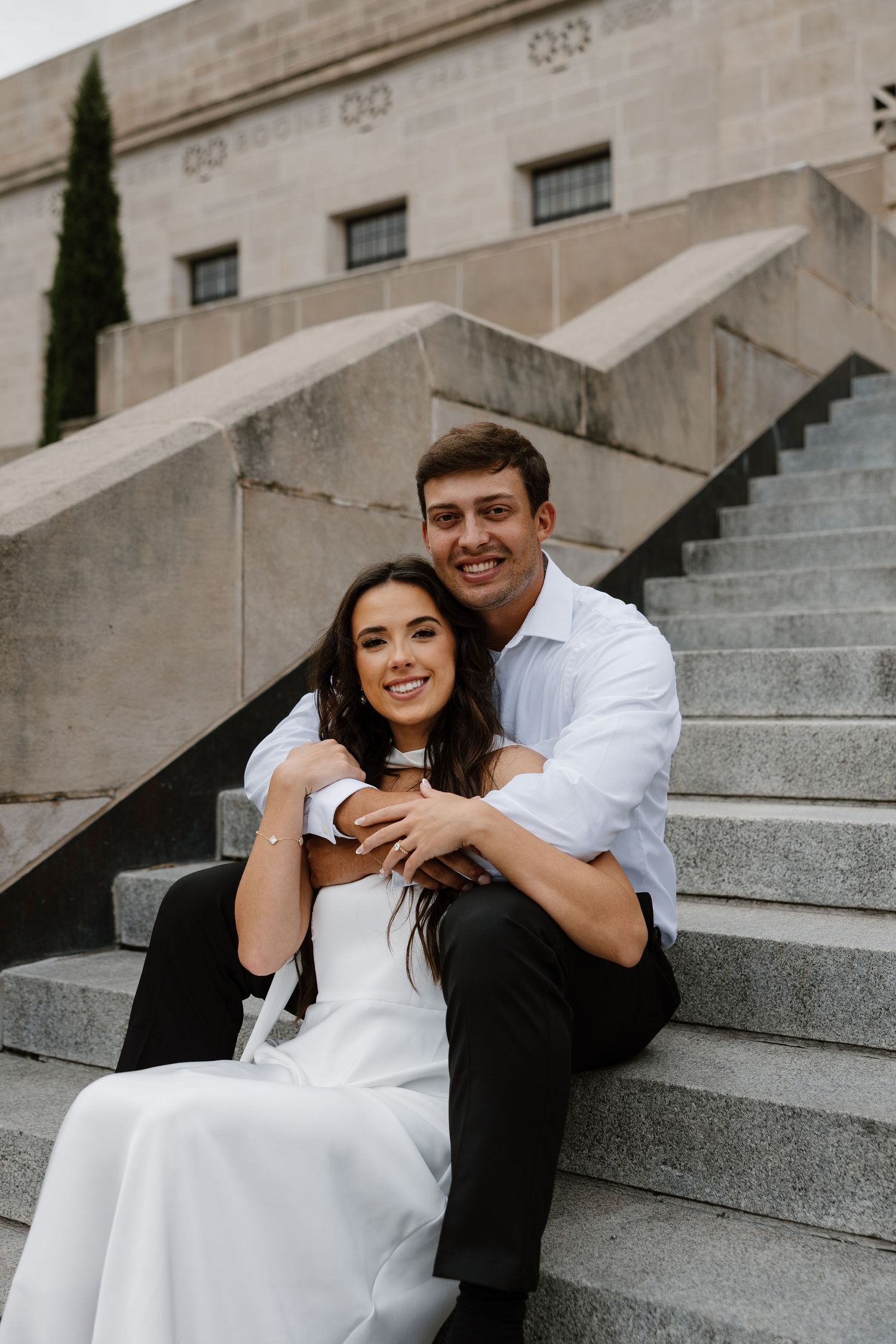 A romantic couple shares tender moments while sitting on stone steps of a grand building.
