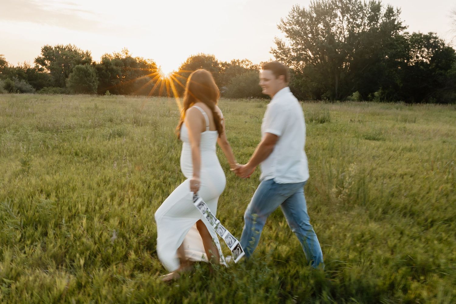 Couple walking hand in hand through sunlit meadow at golden hour.