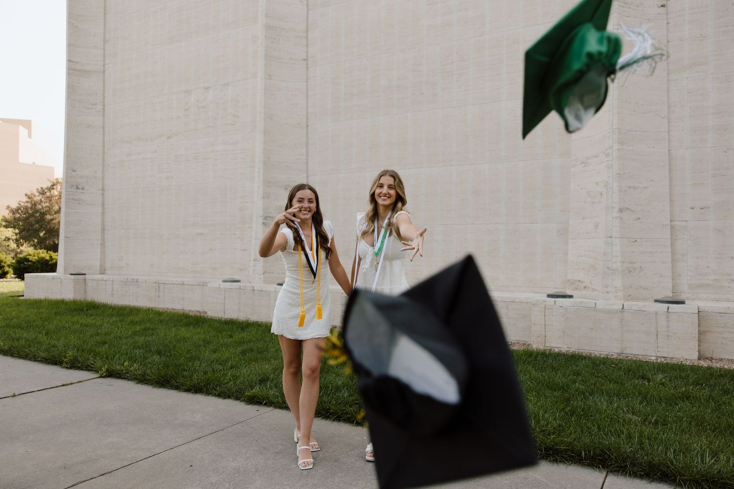 Graduation celebration with caps being tossed in front of white building.