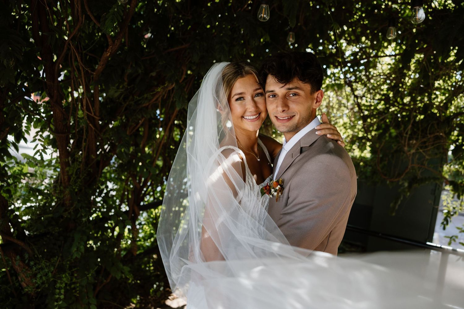 Newlyweds share joyful moments under green foliage on their wedding day.