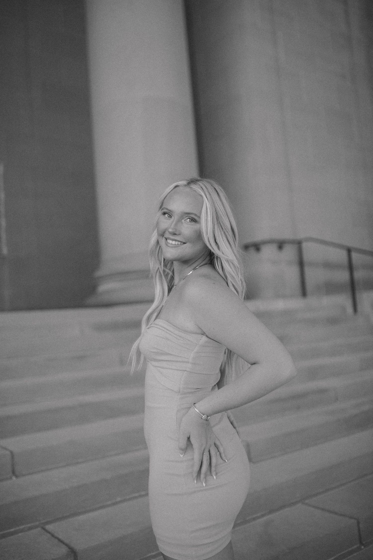 Black and white portrait of a woman posing on stone steps in a fitted dress.