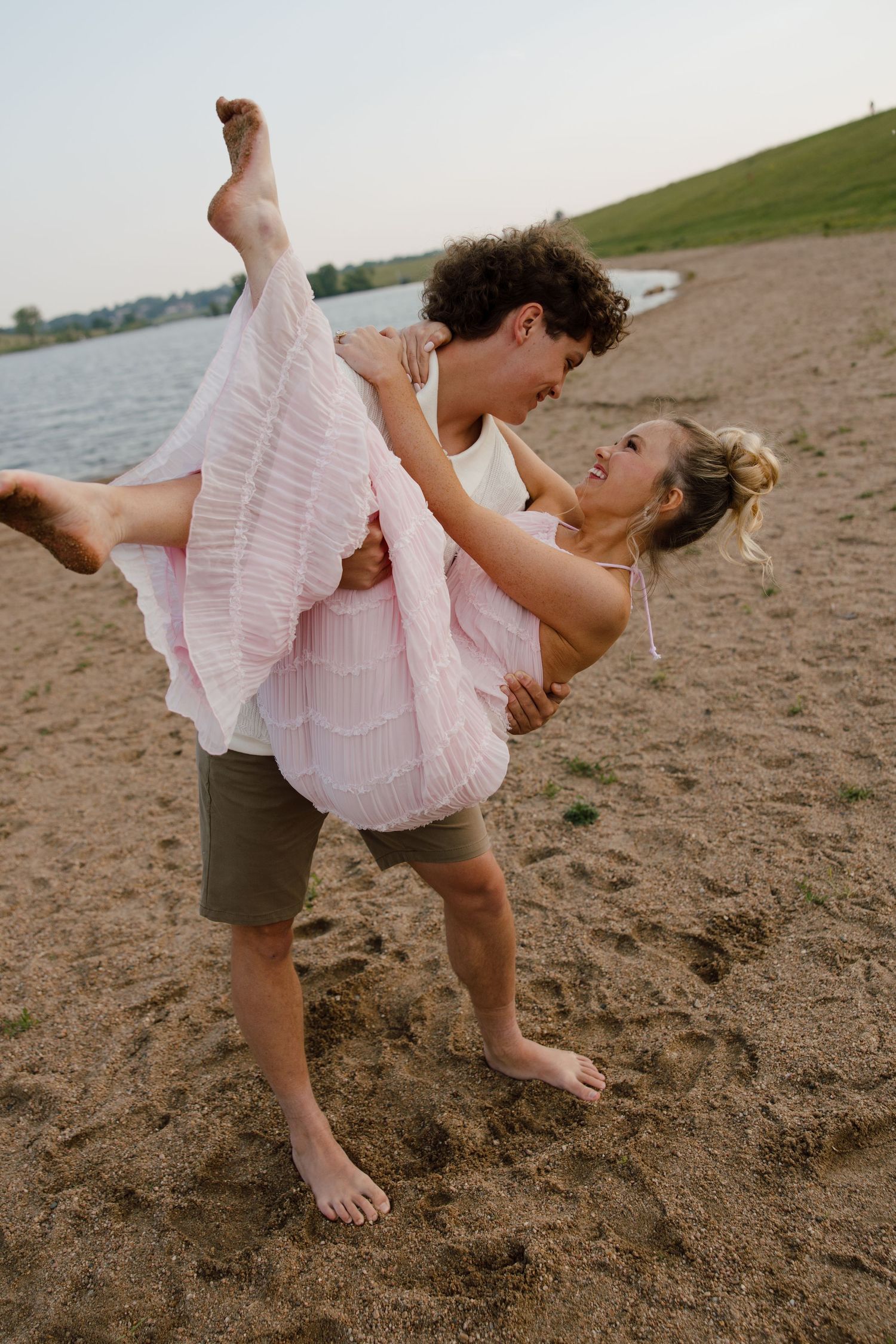 A romantic moment captured on a beach as a couple embraces in playful pose at sunset.