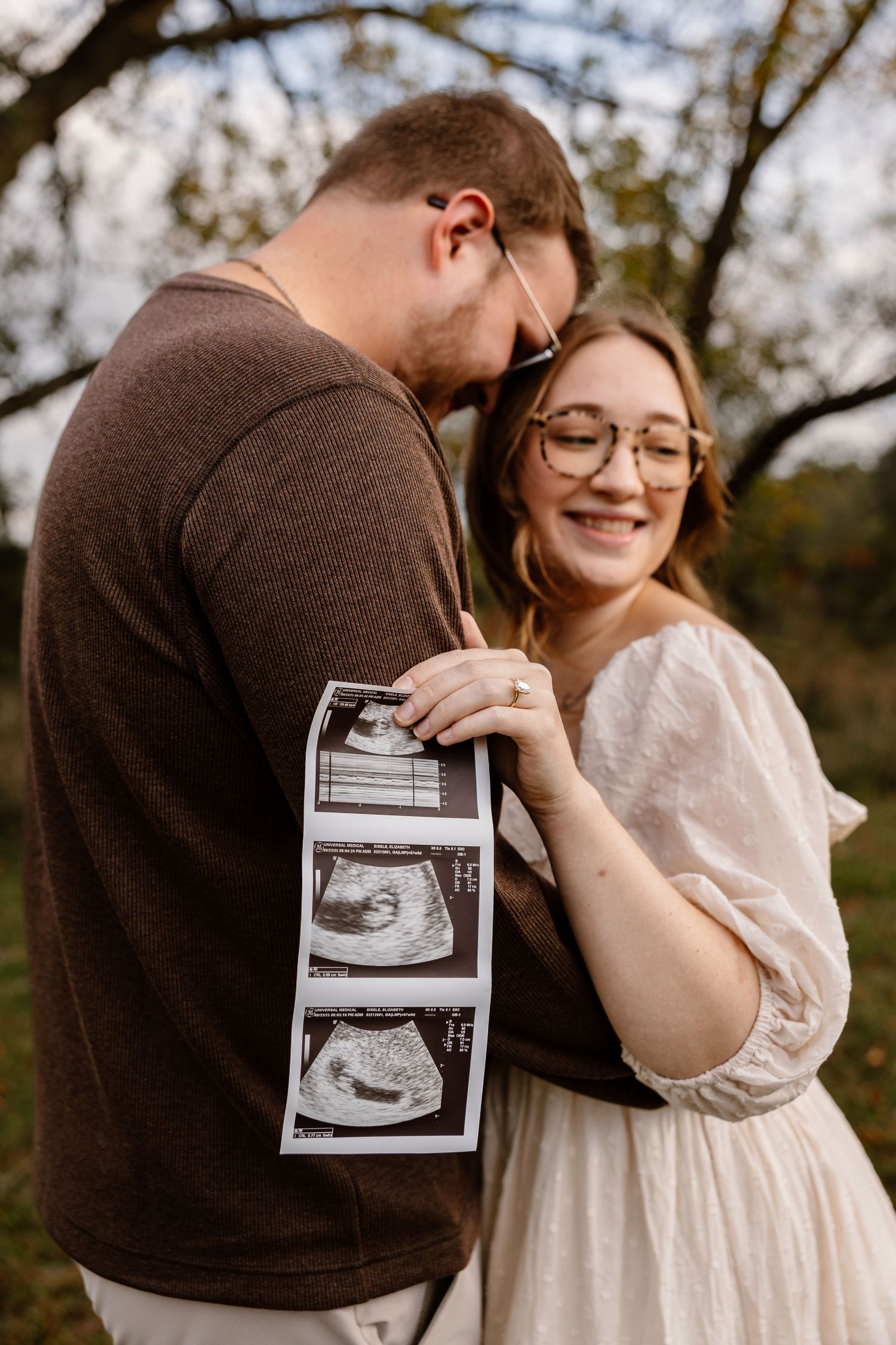 Couple holding ultrasound photos during outdoor pregnancy announcement photoshoot.