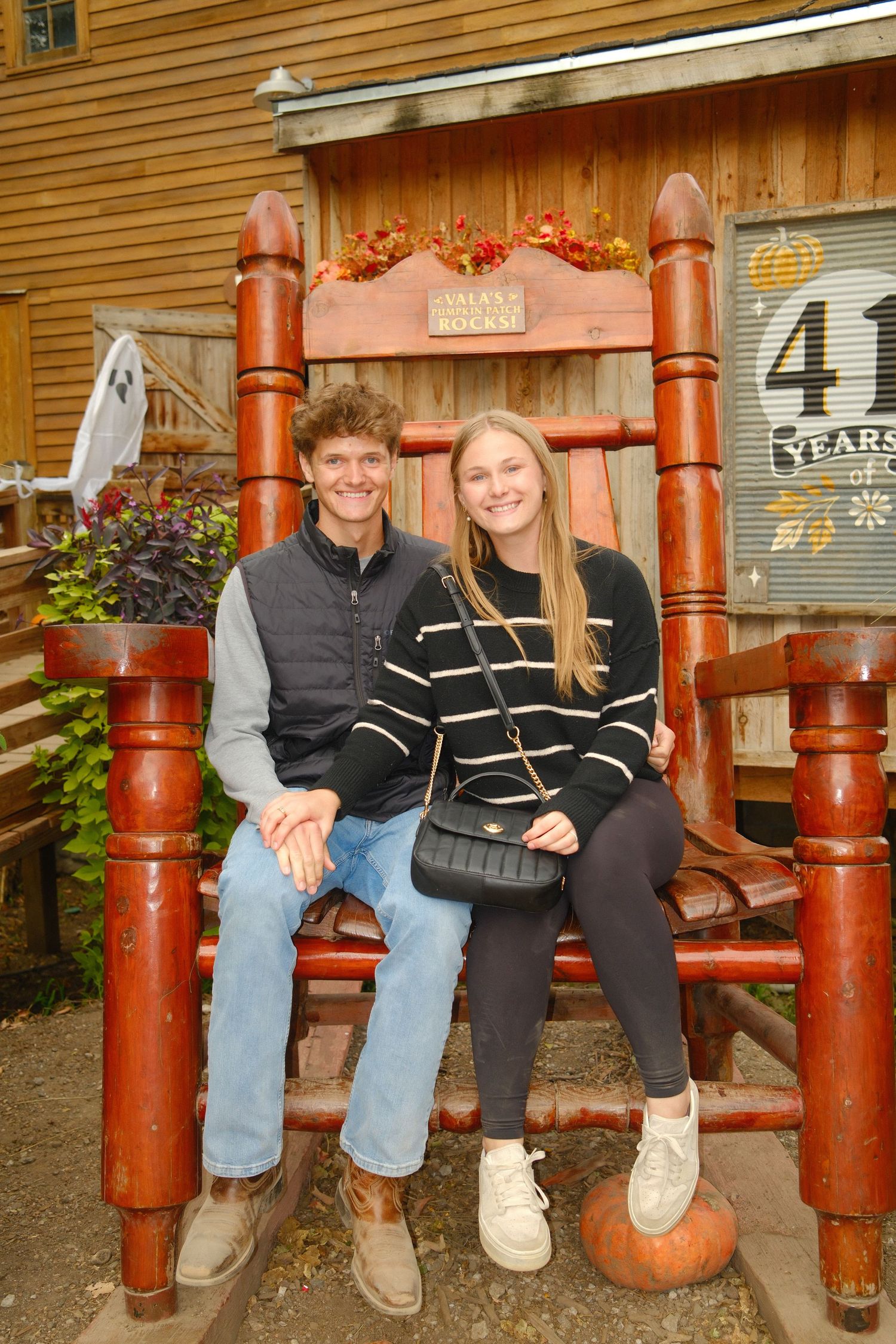A large decorative wooden bench with fall decorations outside a rustic building.