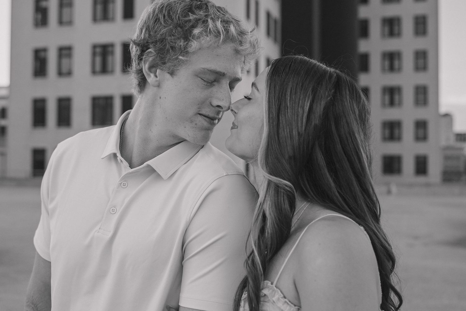 A romantic black and white portrait of a couple sharing an intimate moment against an urban backdrop.