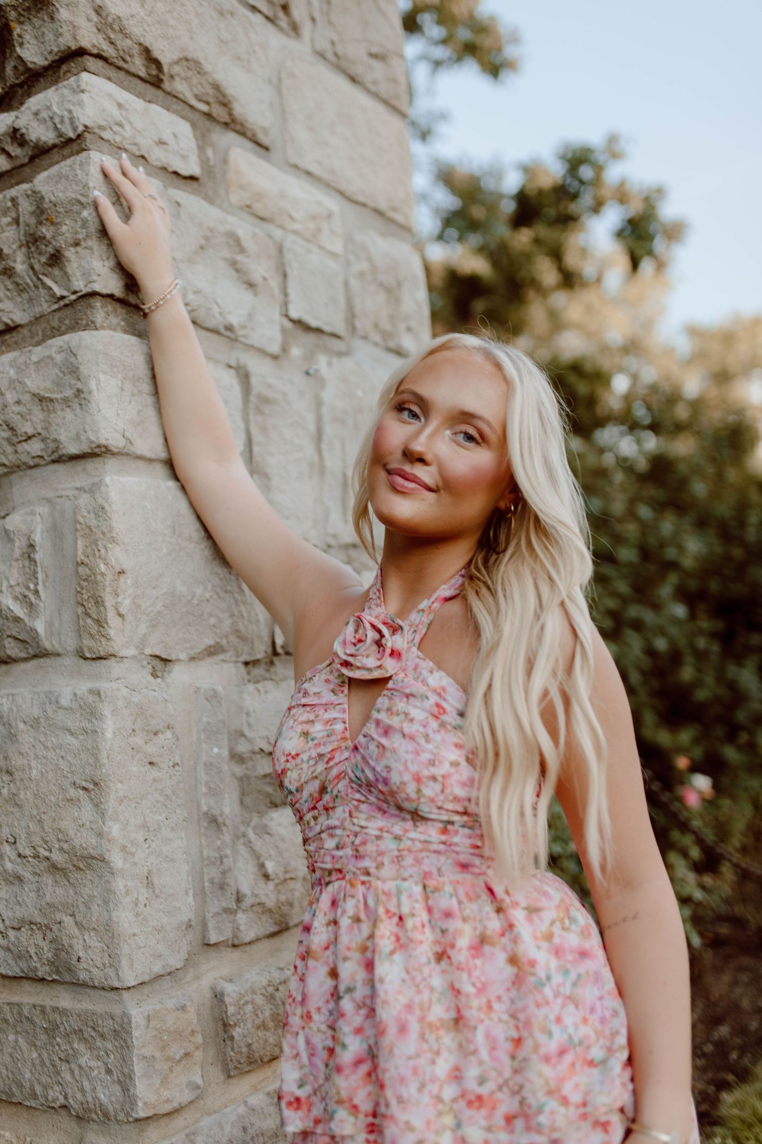 A summer portrait against a stone wall wearing a pink floral dress.
