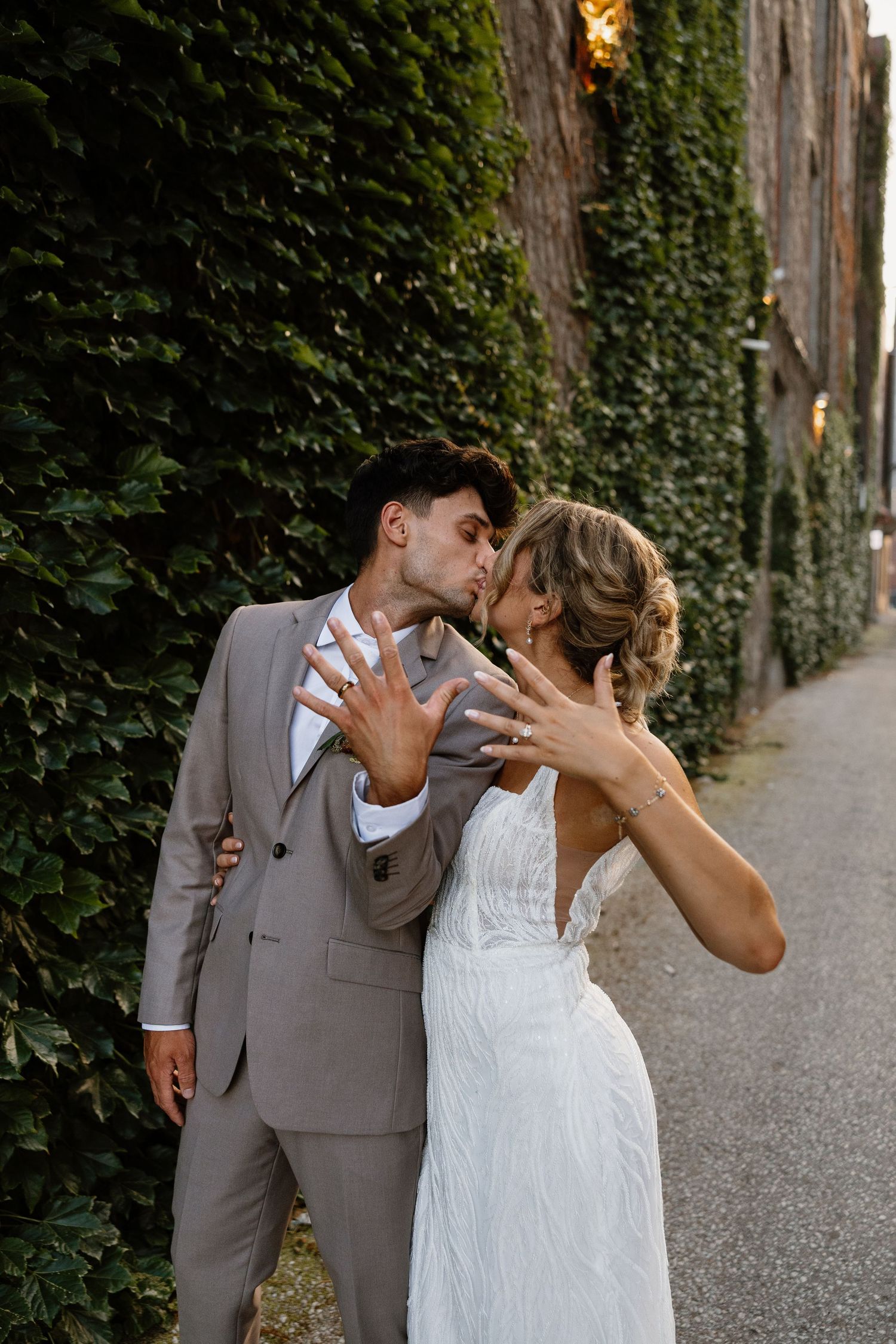 Newlywed couple in wedding attire sharing playful moments along an ivy-covered path.