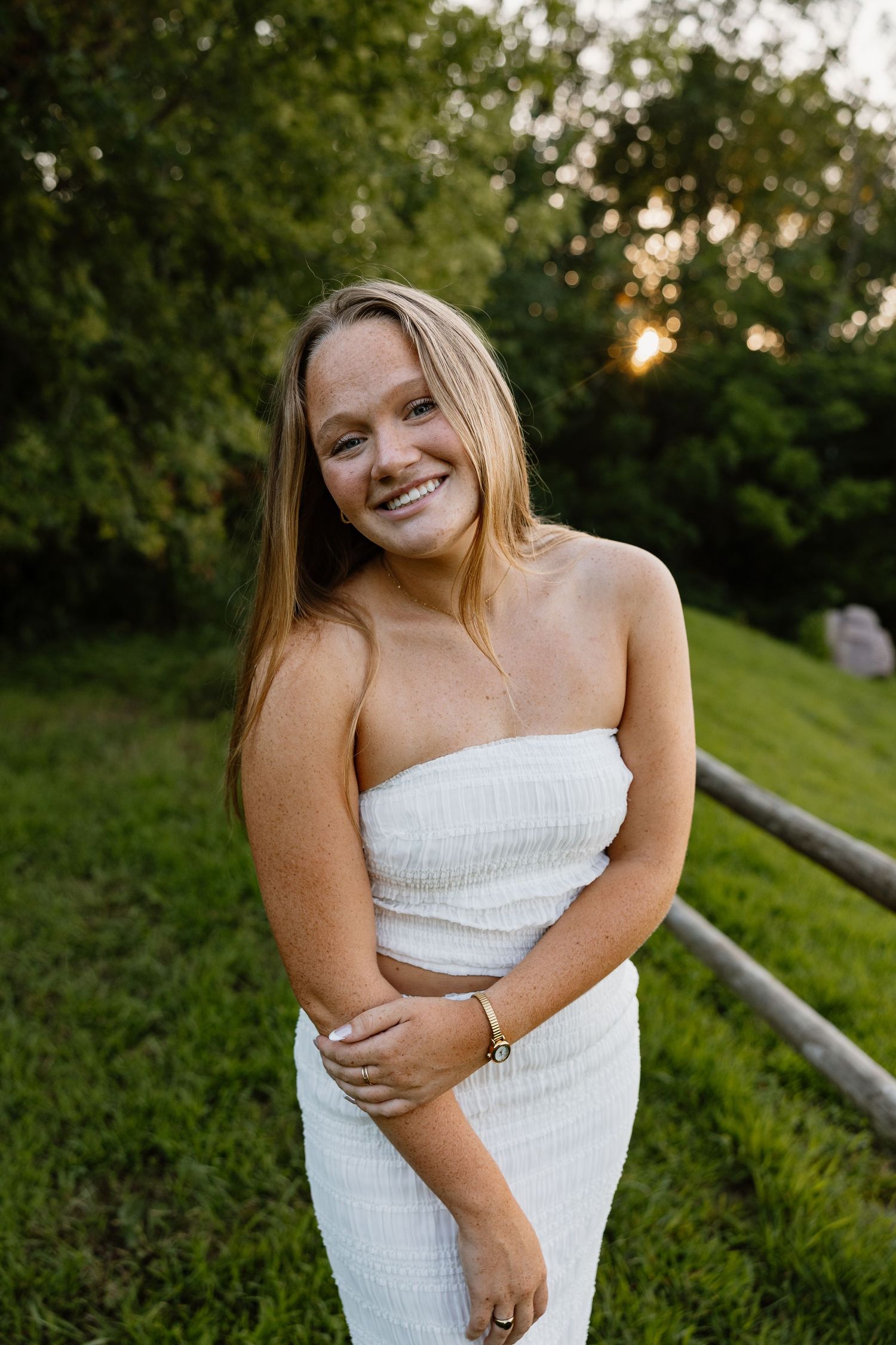 Summer portrait session on grassy hill with wooden fence at sunset.