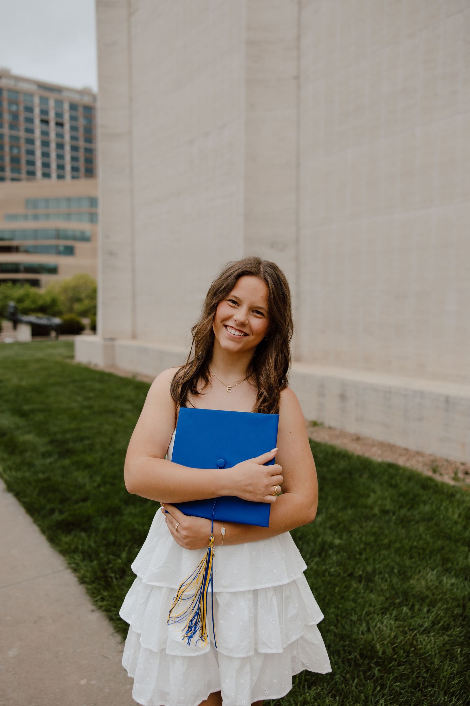 Graduate in white dress hugging blue graduation gown outdoors.