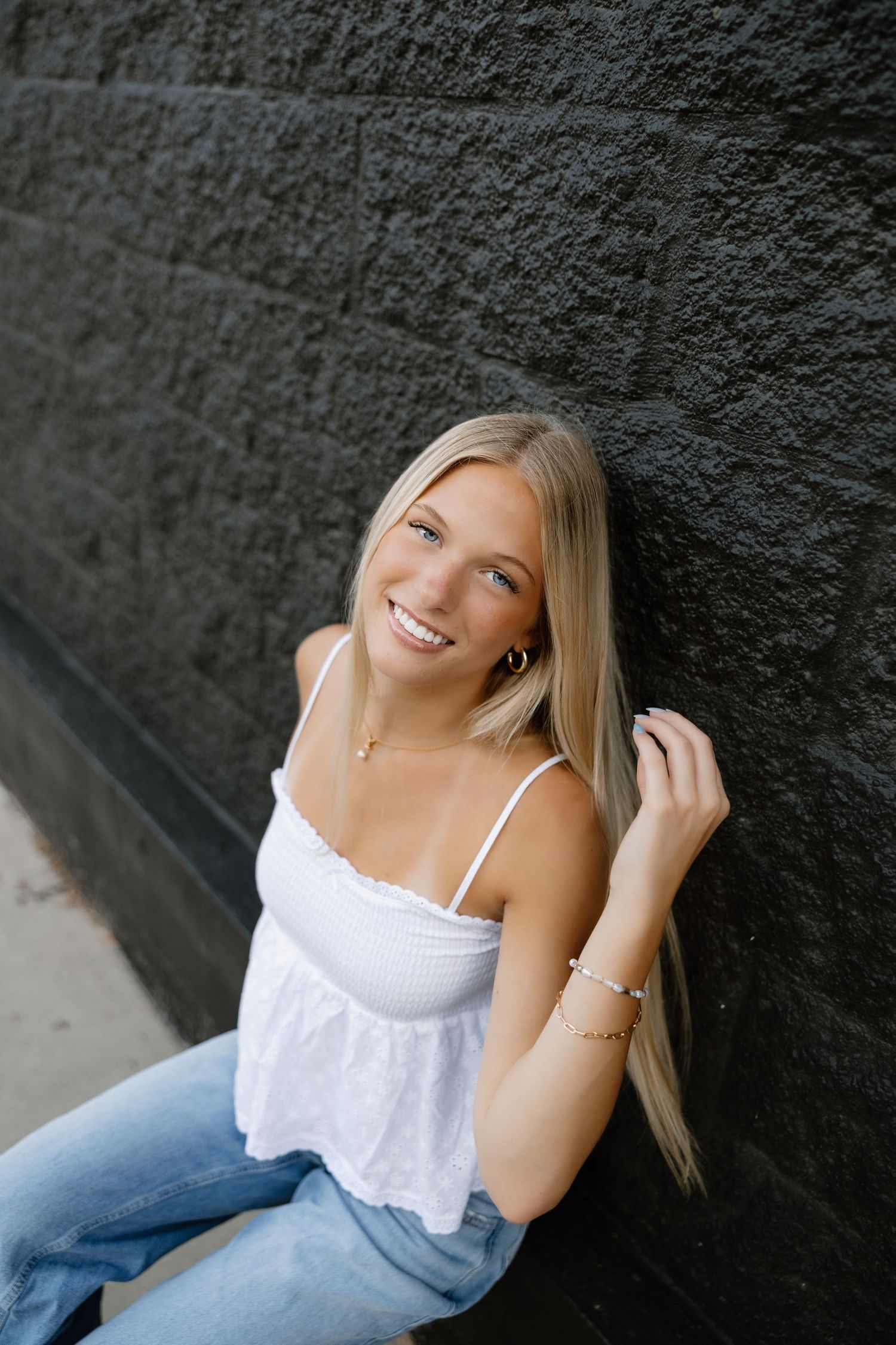 Casual portrait session against dark textured wall wearing white top and denim.