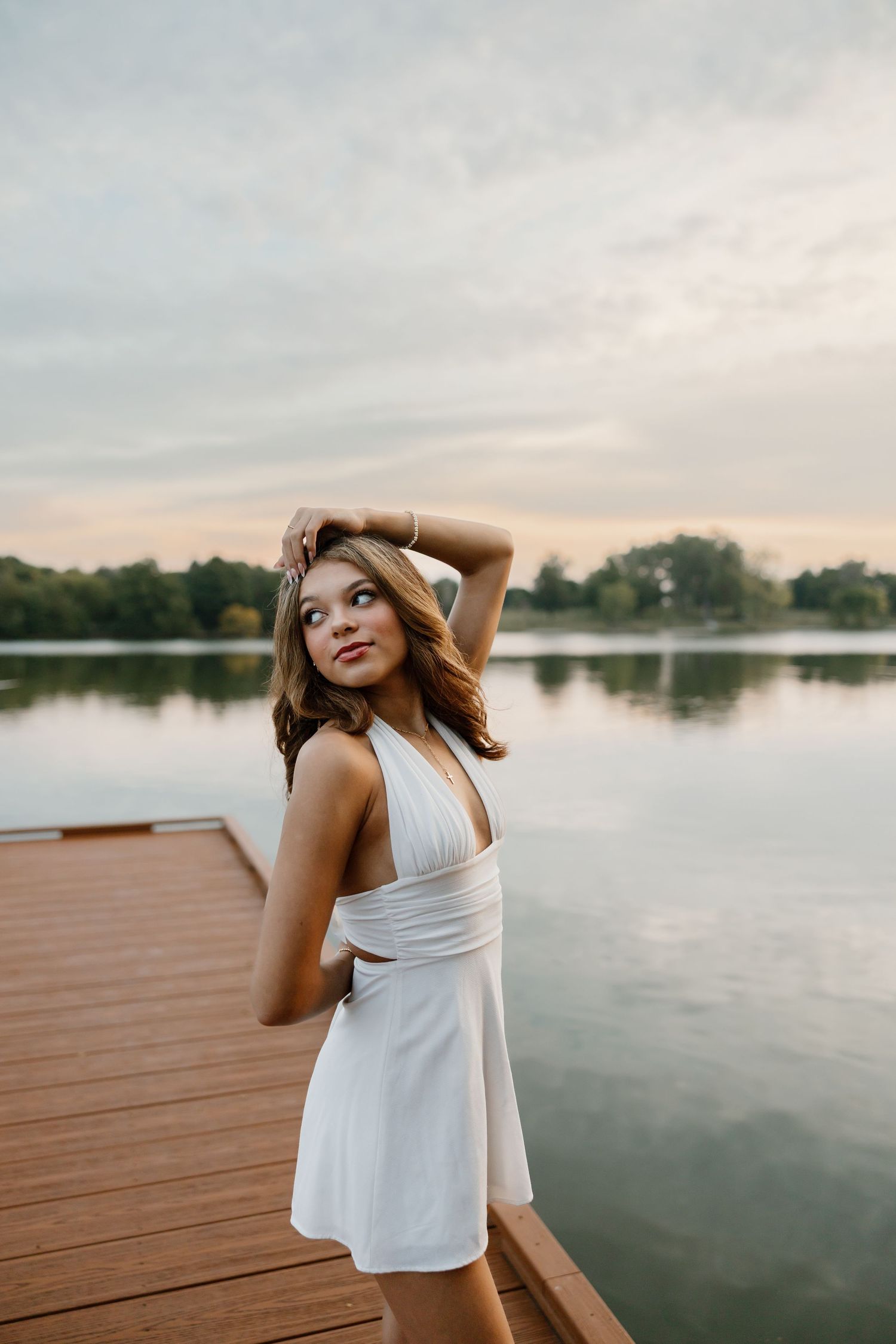 A woman in a white sundress poses on a wooden dock during golden hour.