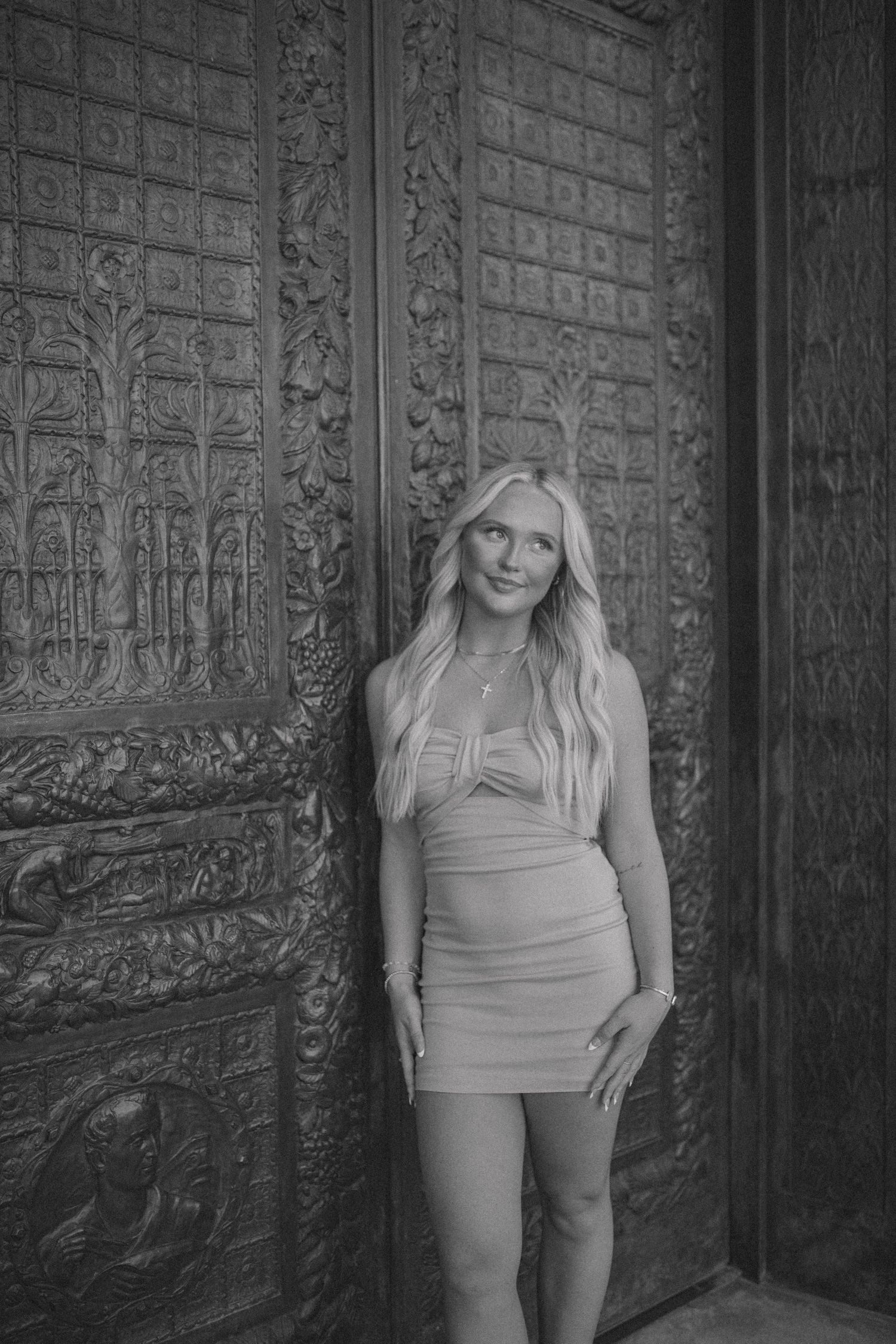 Woman in form-fitting dress poses against an ornately carved vintage door.