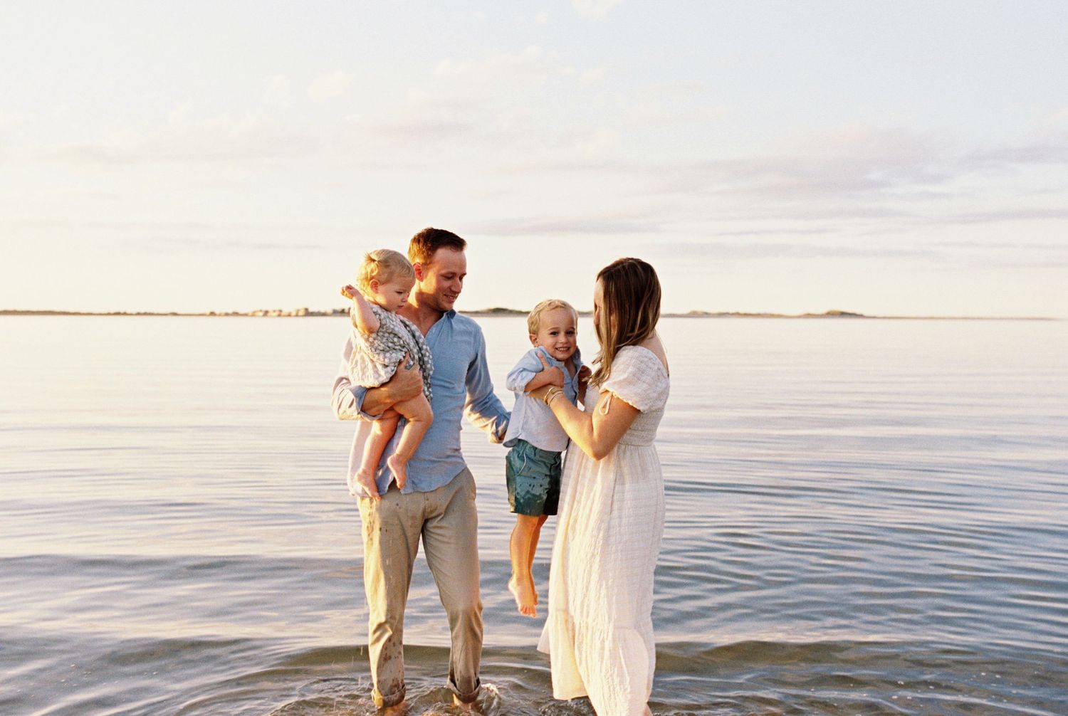 Family enjoying a sunset walk along the beach shore with soft waves and golden light.