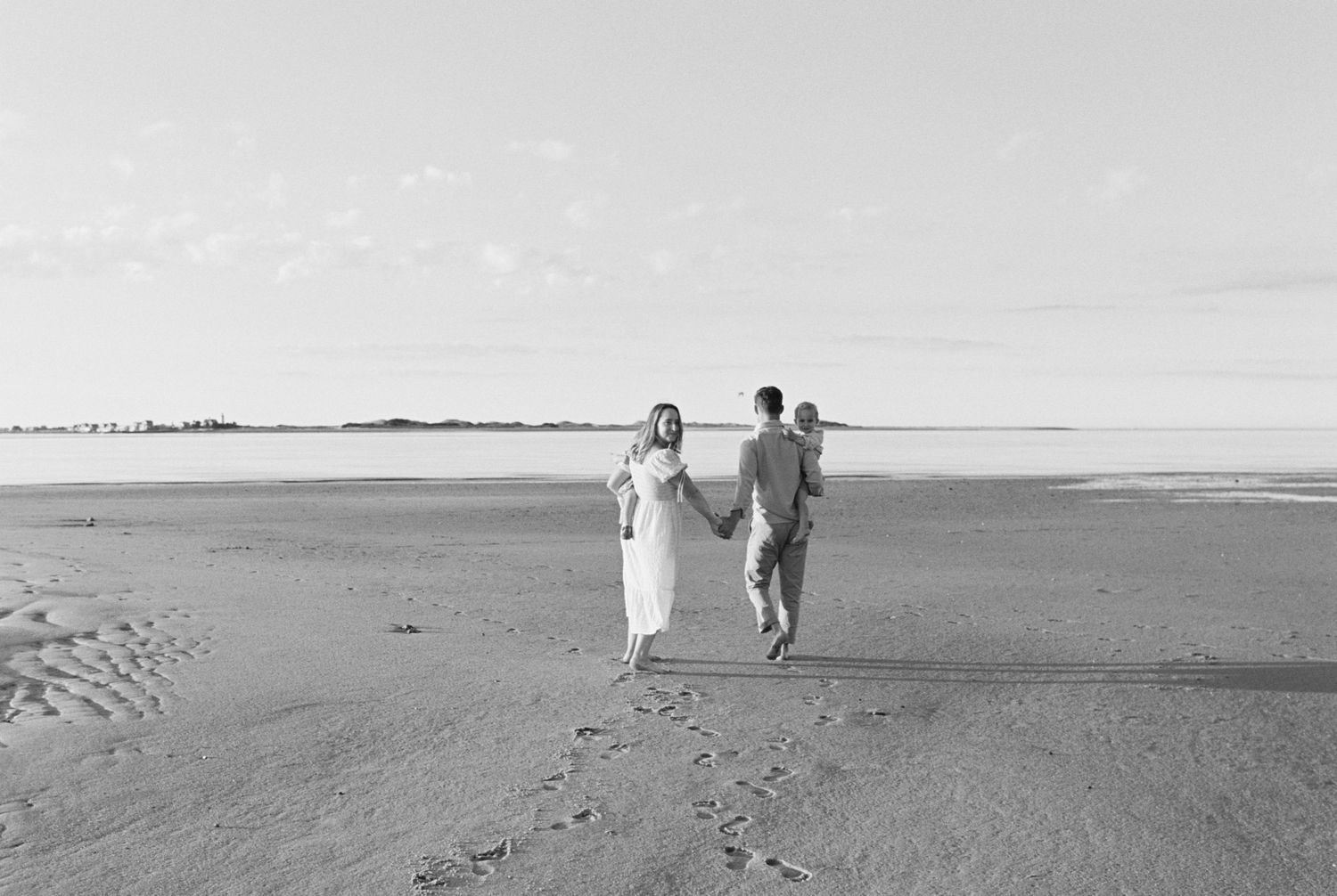 Black and white photo of people walking along expansive empty beach with distant horizon.