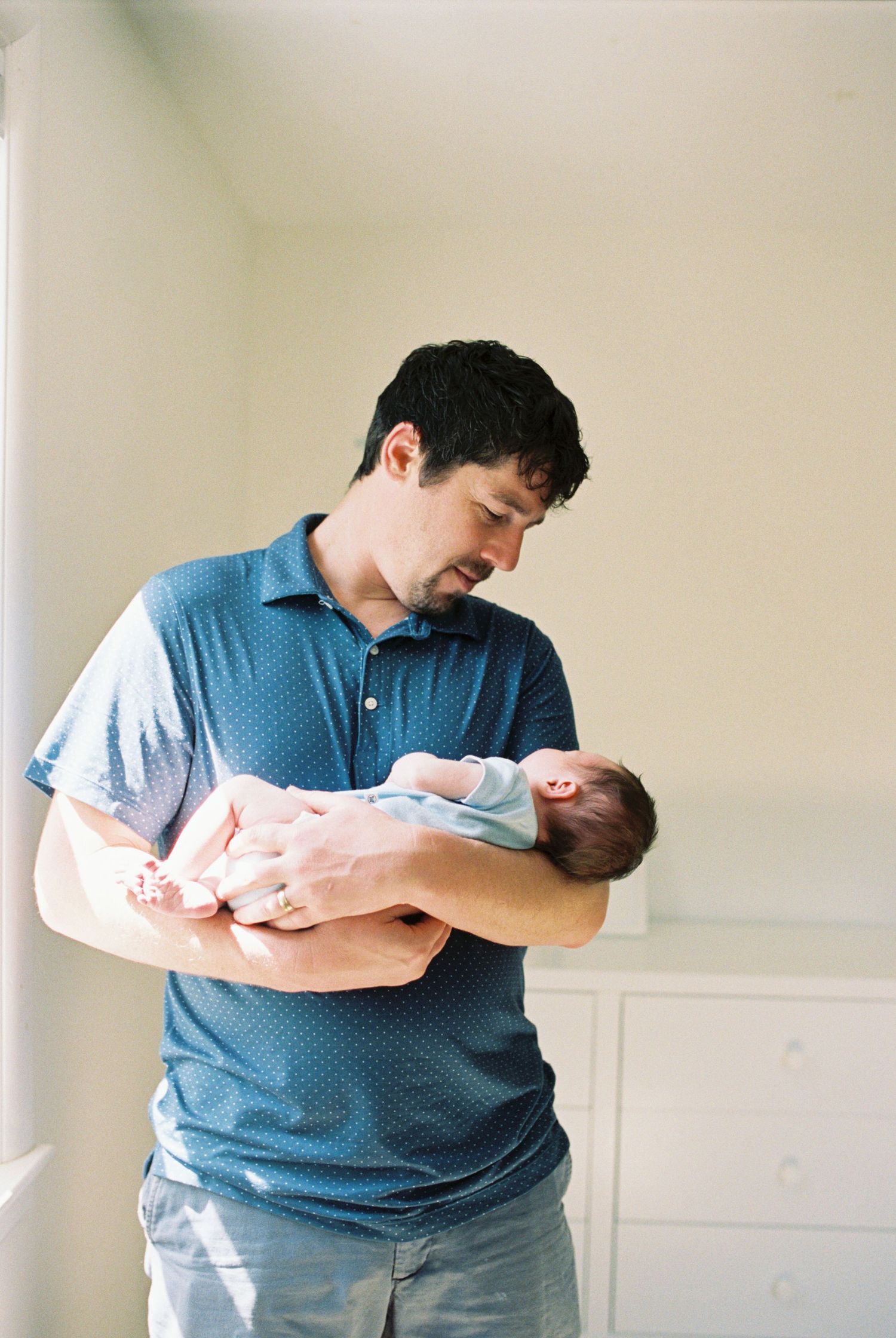 Parent in blue shirt cradling and bonding with newborn baby.