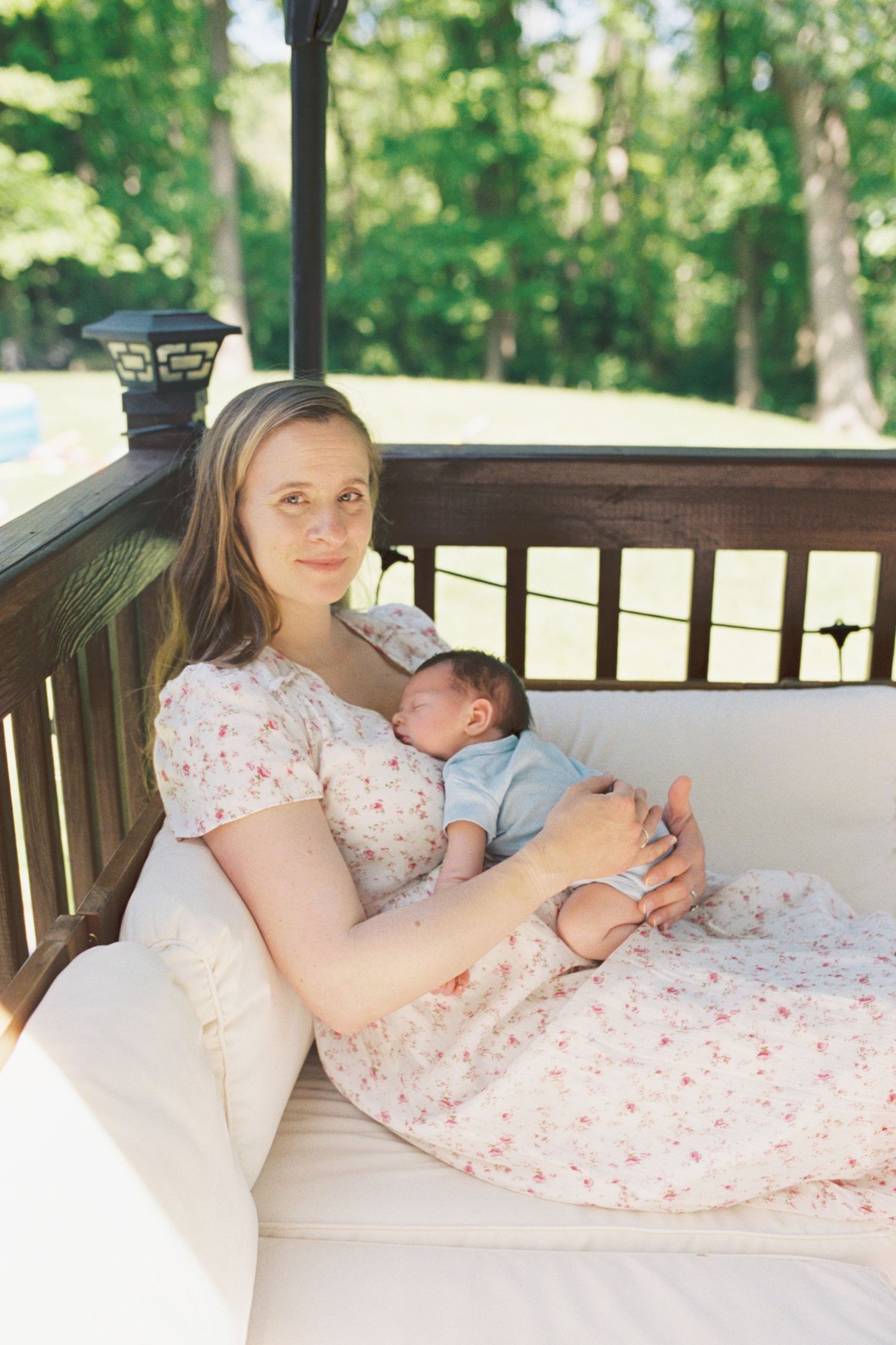 Family relaxing together on outdoor porch bench with newborn baby.