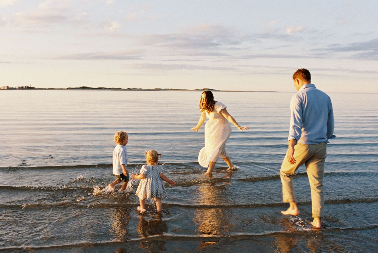 Family wading through shallow ocean water during golden hour at beach.