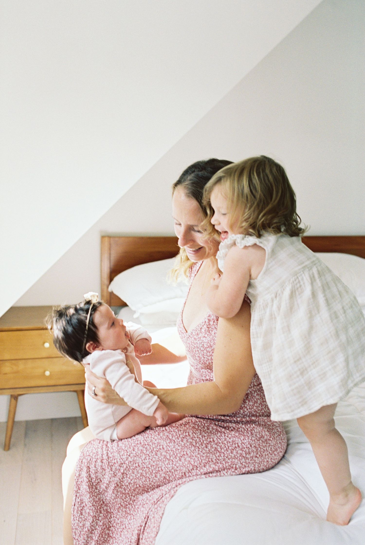 Family bonding moments on a white bed in soft natural light.