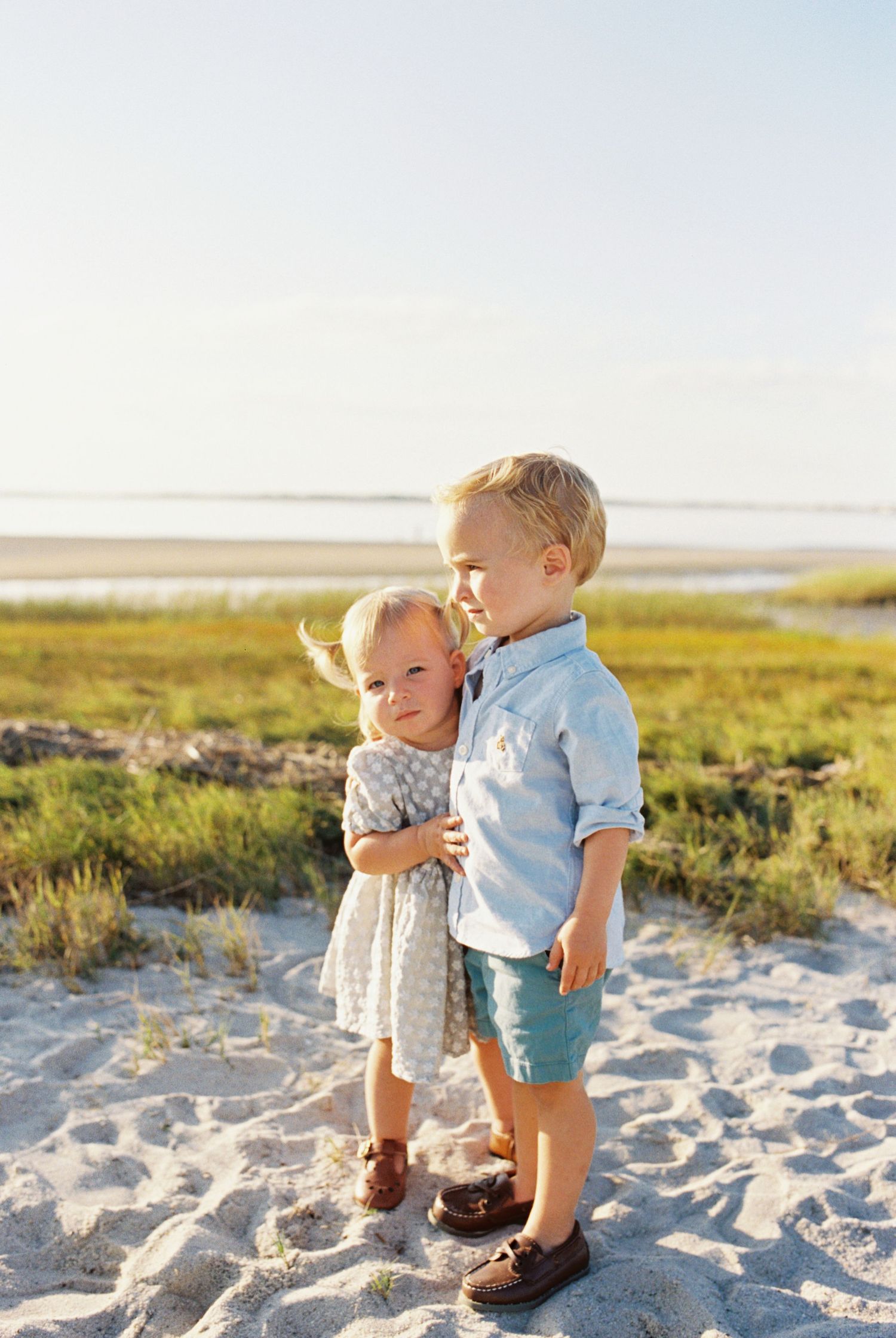 Two small children explore and play together on a sandy beach during golden hour at sunset.