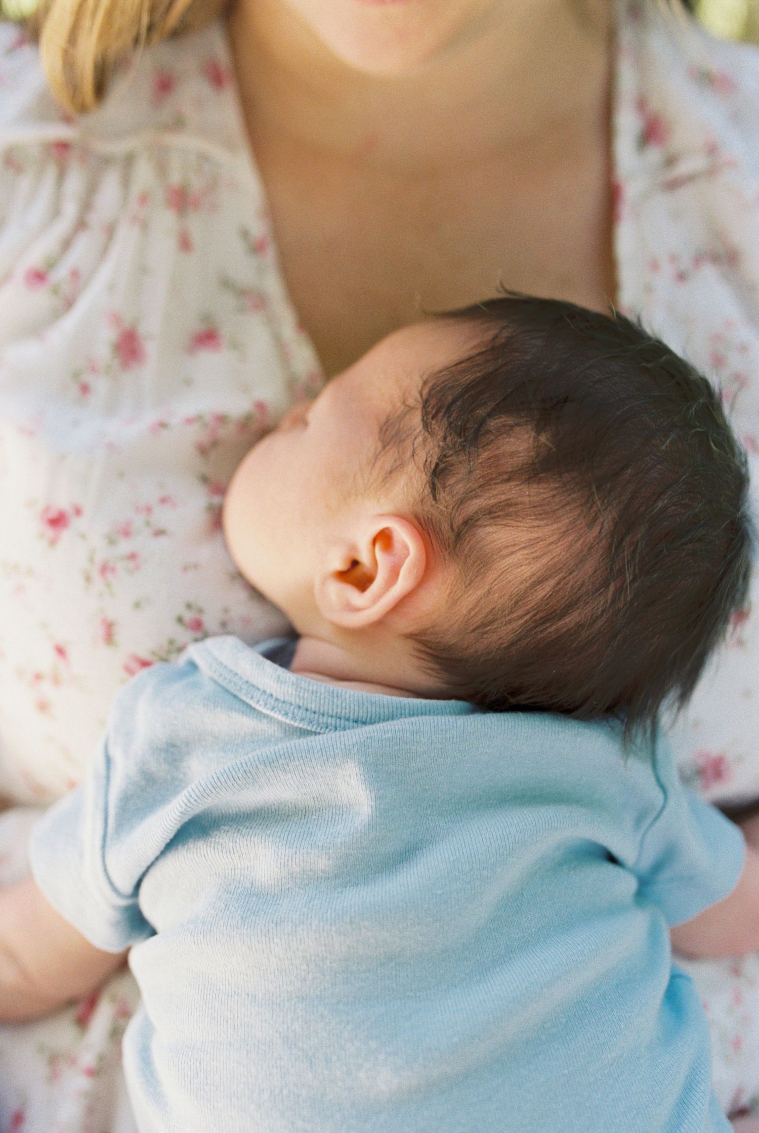 Infant in light blue shirt rests against floral dress fabric.