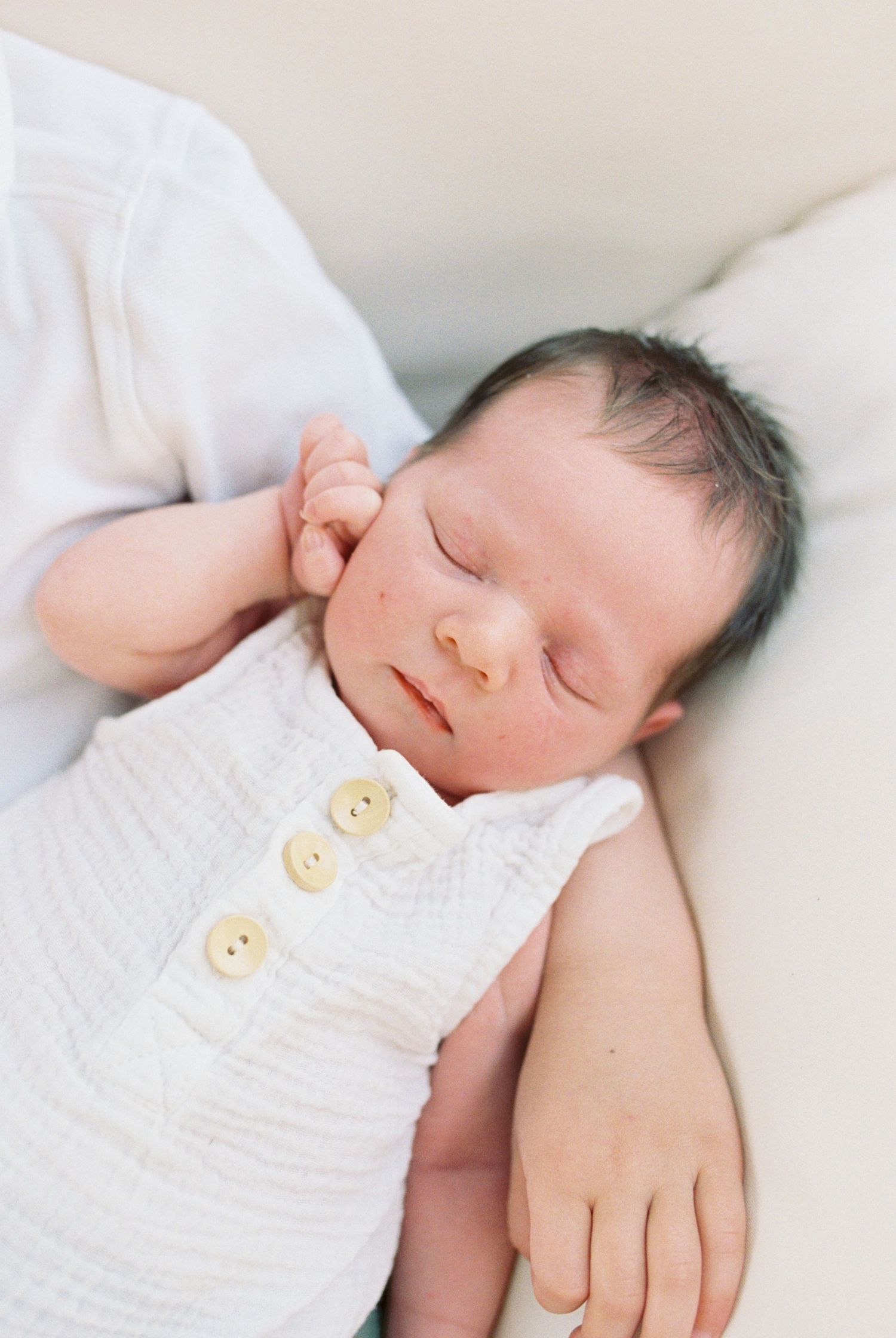 A sleeping newborn baby wearing a white knitted outfit with buttons.