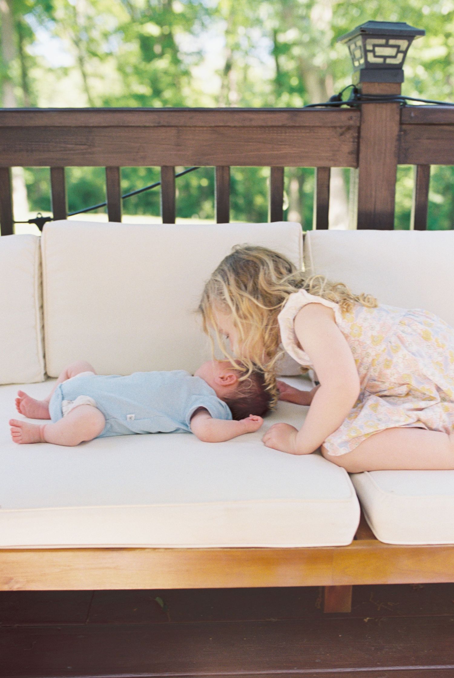 A sweet outdoor moment between siblings on a cushioned porch bench.