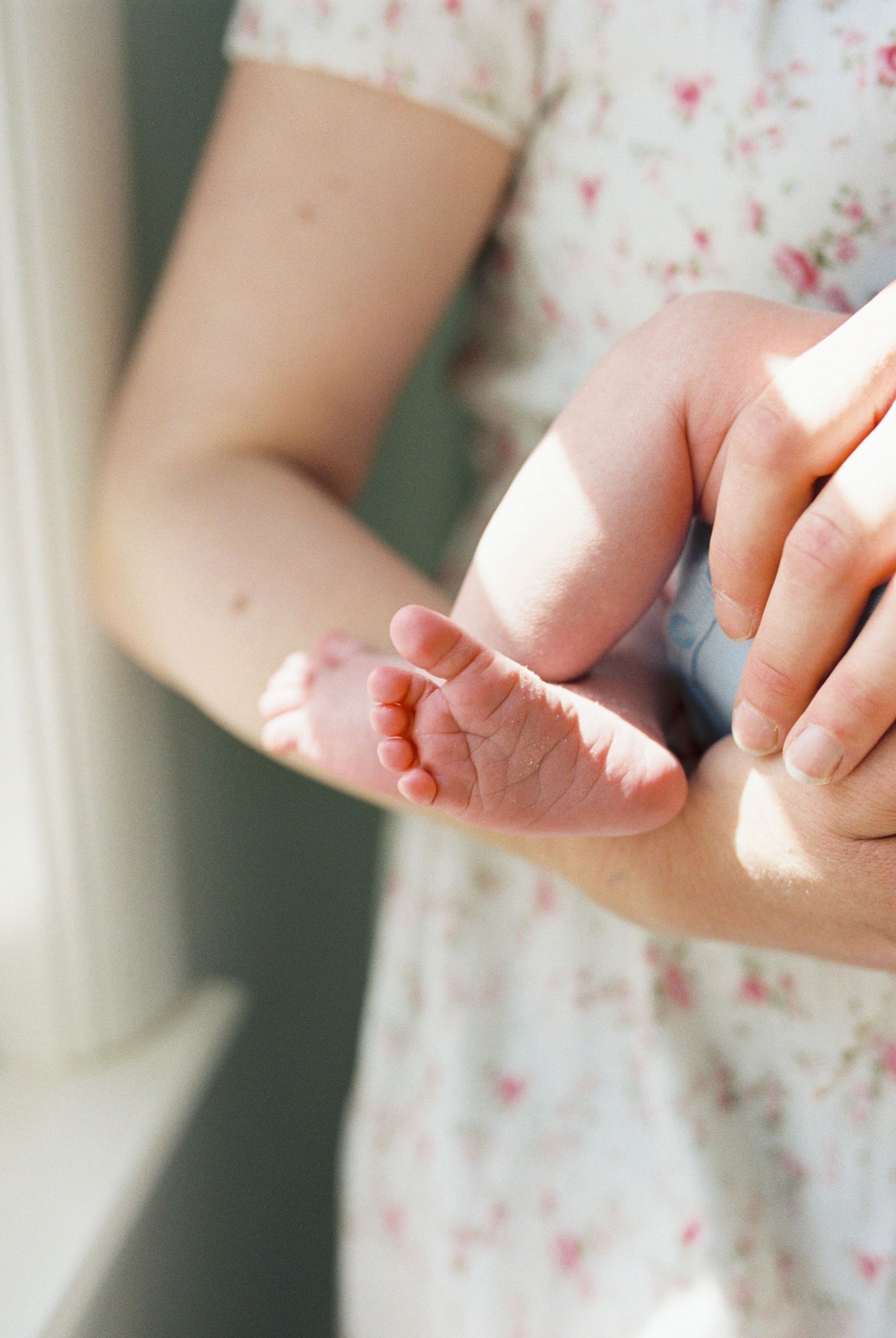 Close-up of tiny newborn feet being gently held in sunlit window light.