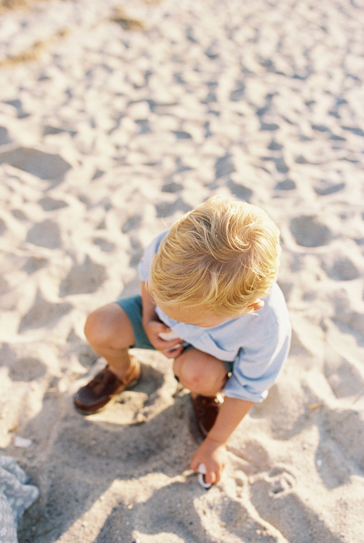 Child playing and digging in soft beach sand during a sunny day.