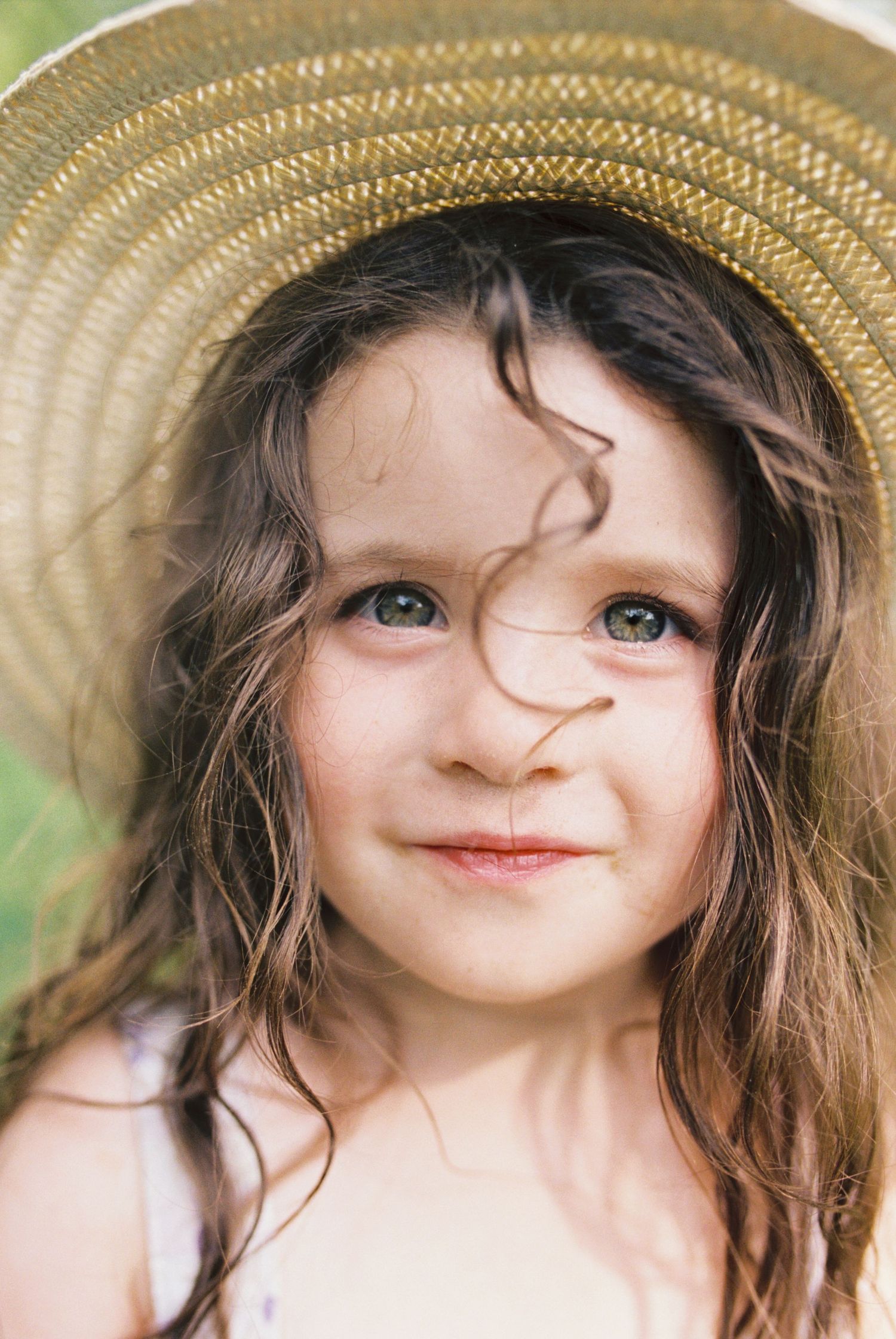 A child wearing a straw hat smiles warmly at the camera in natural lighting.