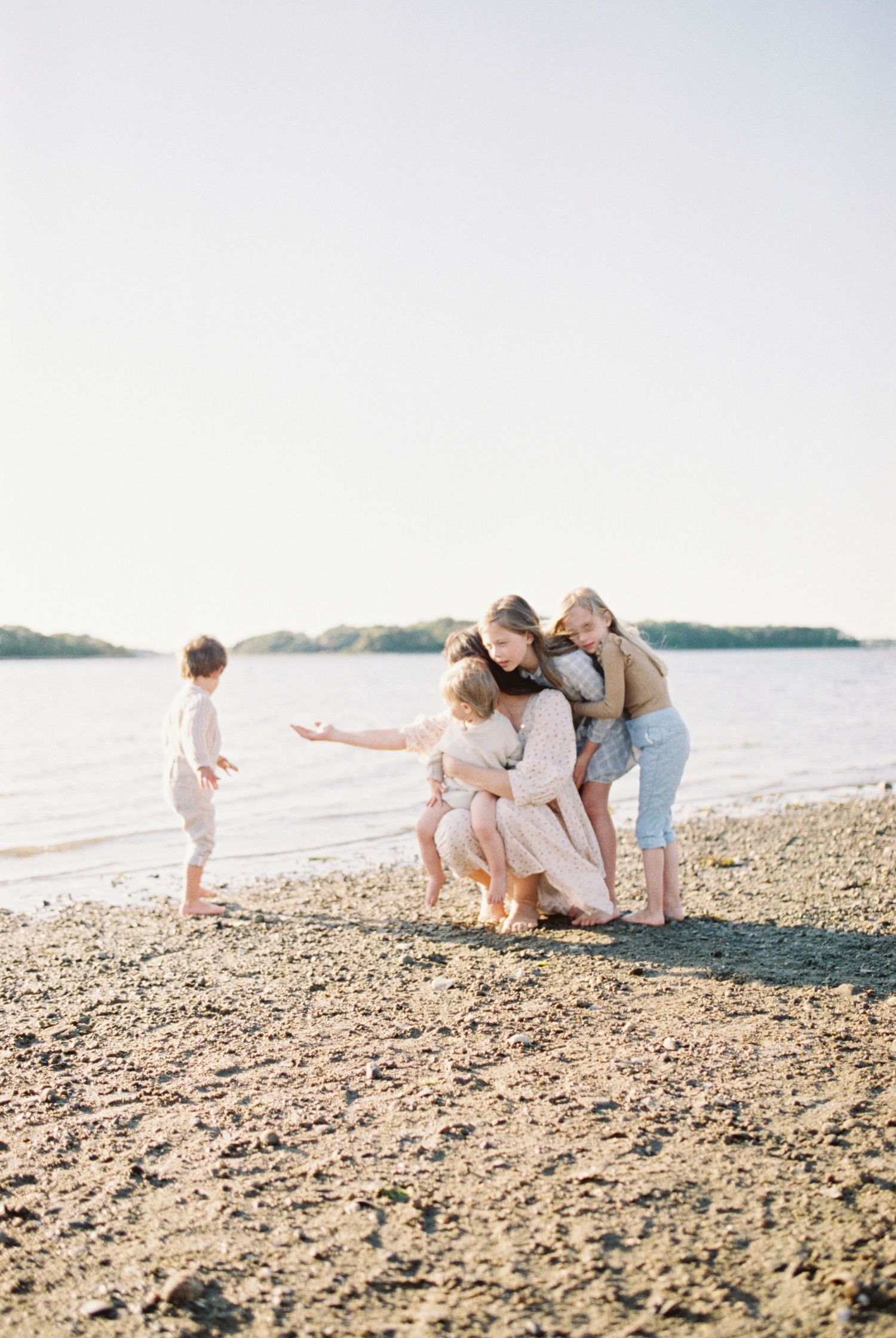 Family exploring and collecting shells together on a rocky beach at sunset.