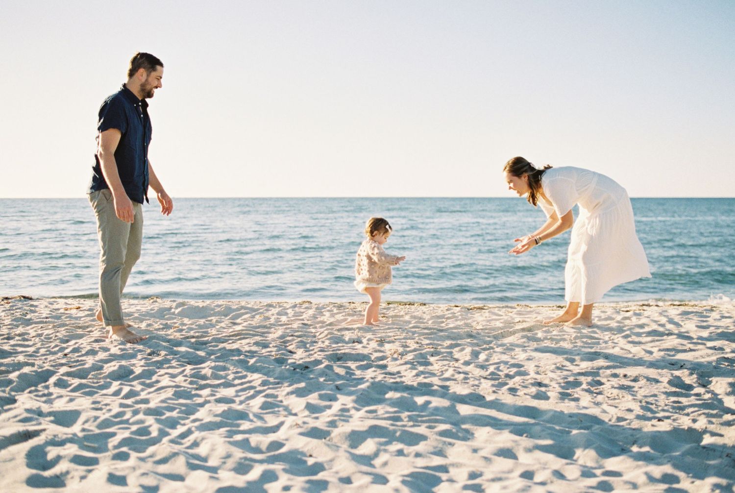 Family members walking and playing together on a pristine beach at sunset.