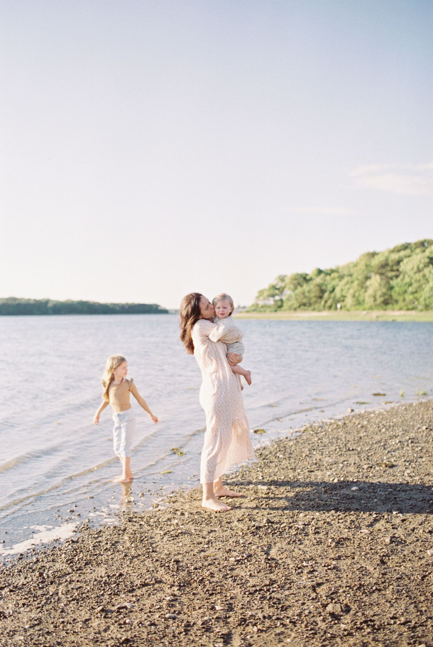 Family enjoying a sunny day together on a rocky beach near water.