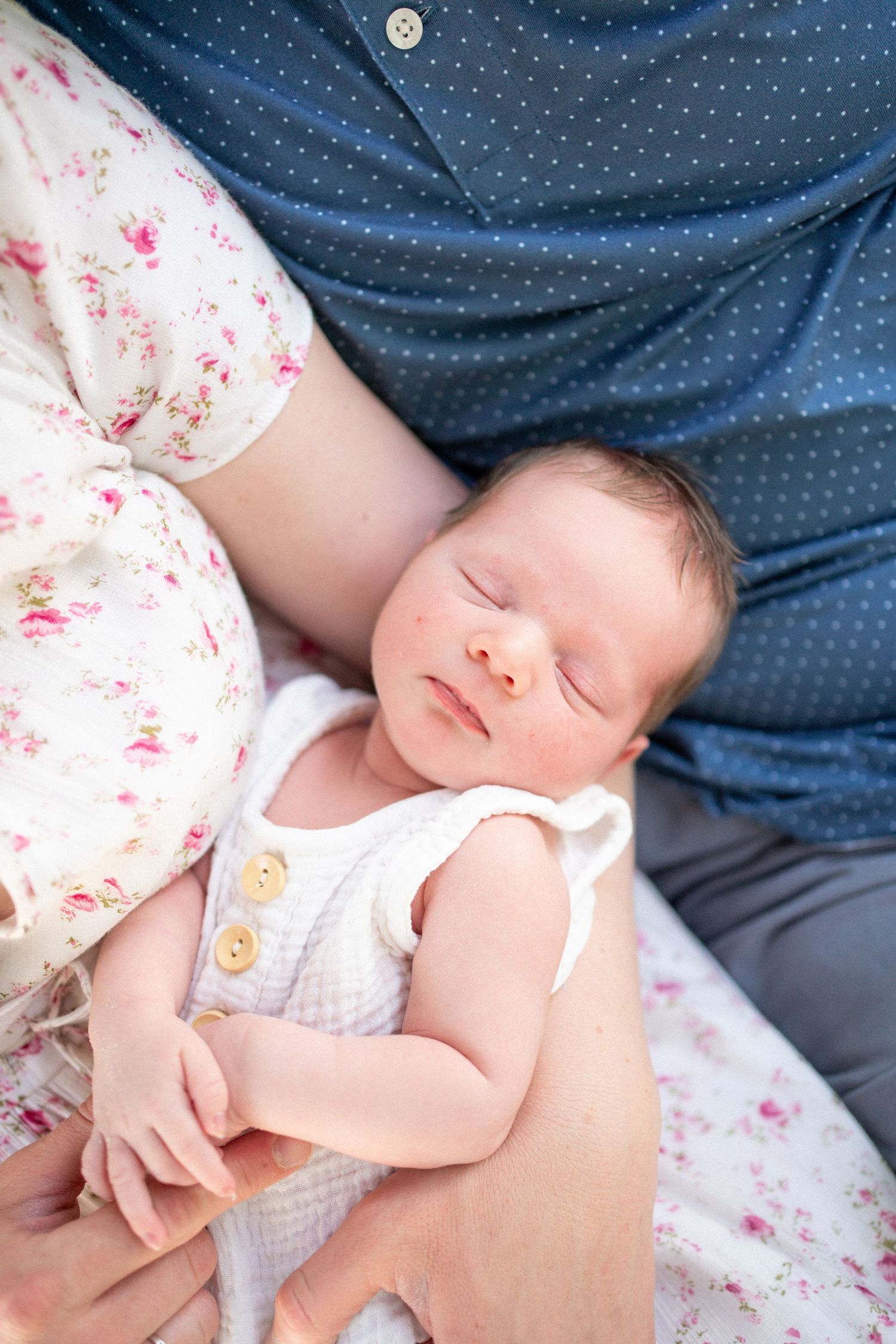 Peaceful newborn resting on polka dot fabric with parent.