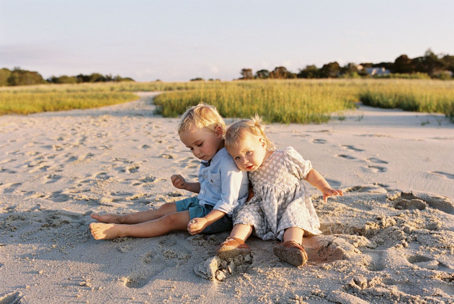 Children playing together in soft beach sand during late afternoon light.