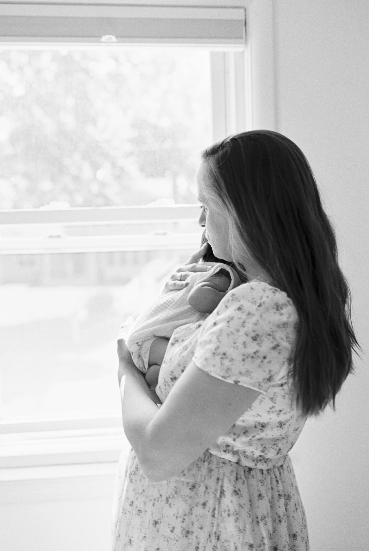 A tender moment between parent and newborn by a bright window in black and white.