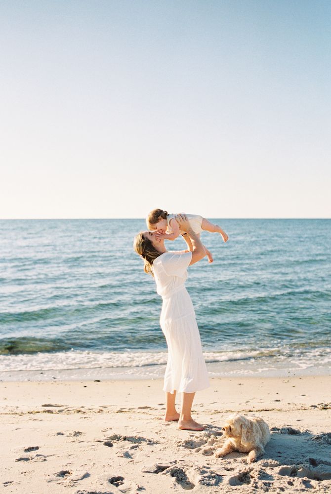 Playful moments captured on a sunny beach with white dresses against blue ocean backdrop.
