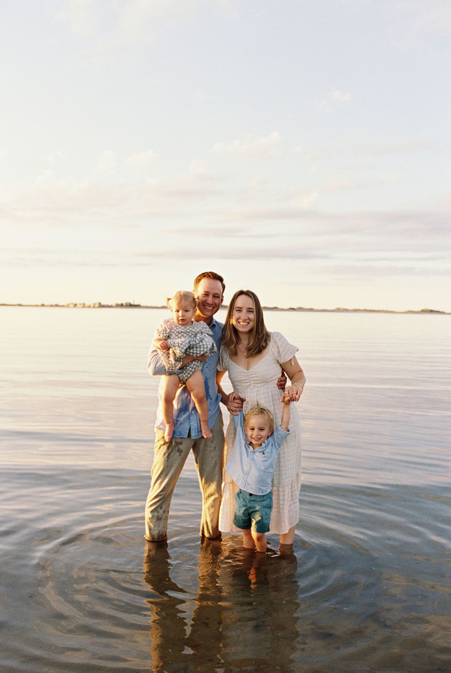 Family enjoying a playful moment together while standing in shallow ocean water at sunset.